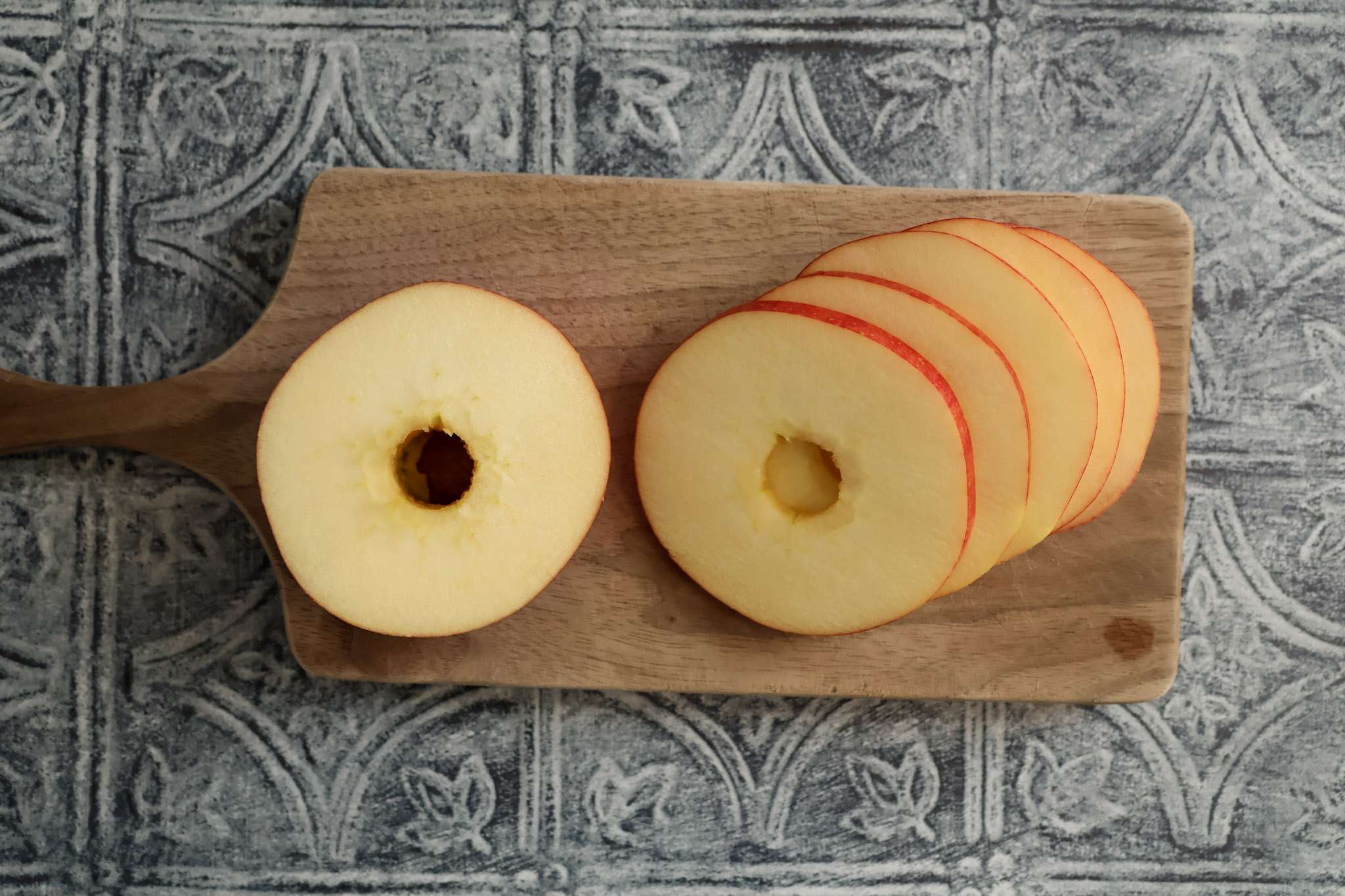 A cored apple sliced into 1/4 inch thick rings on a wooden board