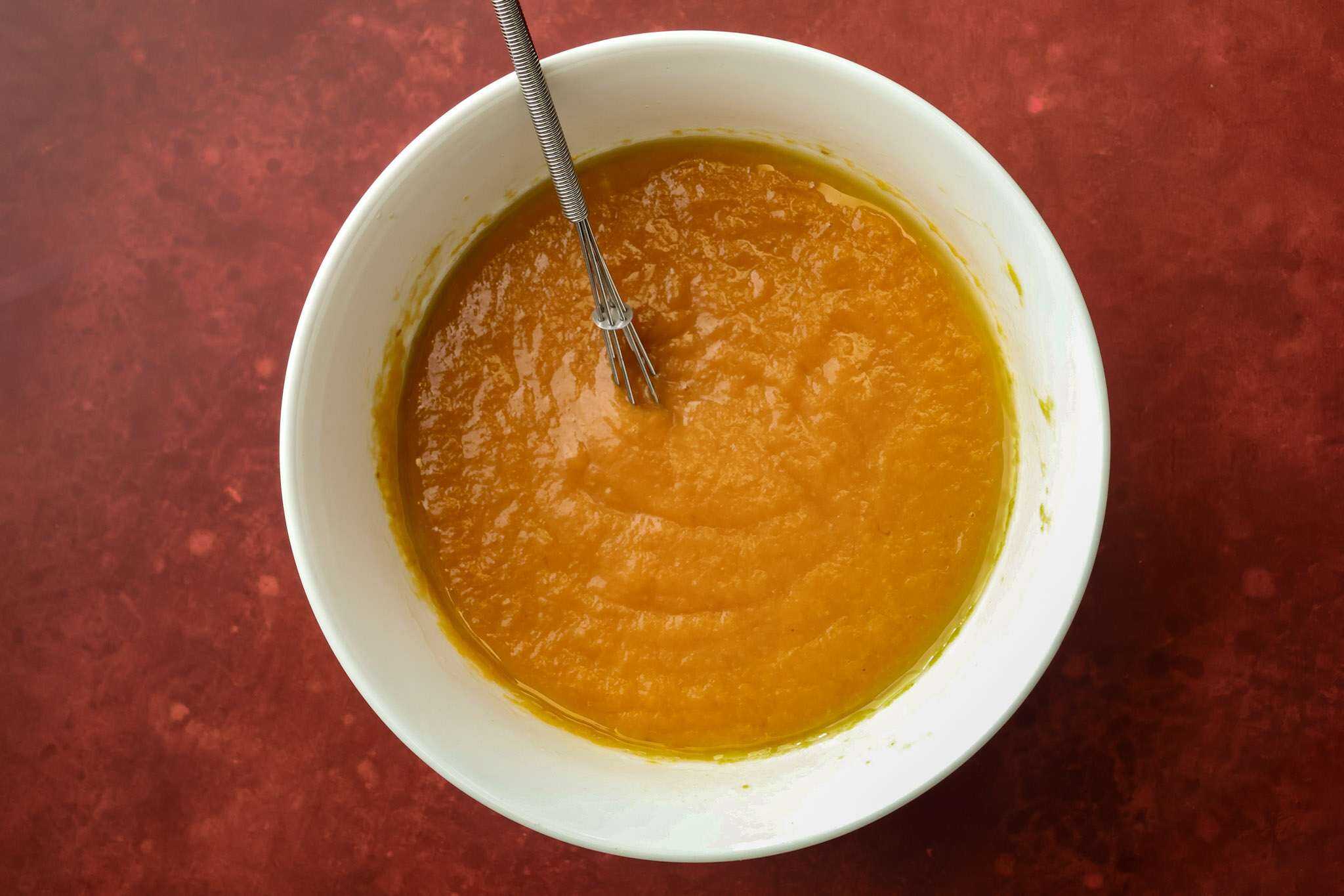 a white bowl on a red surface - the bowl contains the blended wet ingredients for tender gluten-free pumpkin muffins