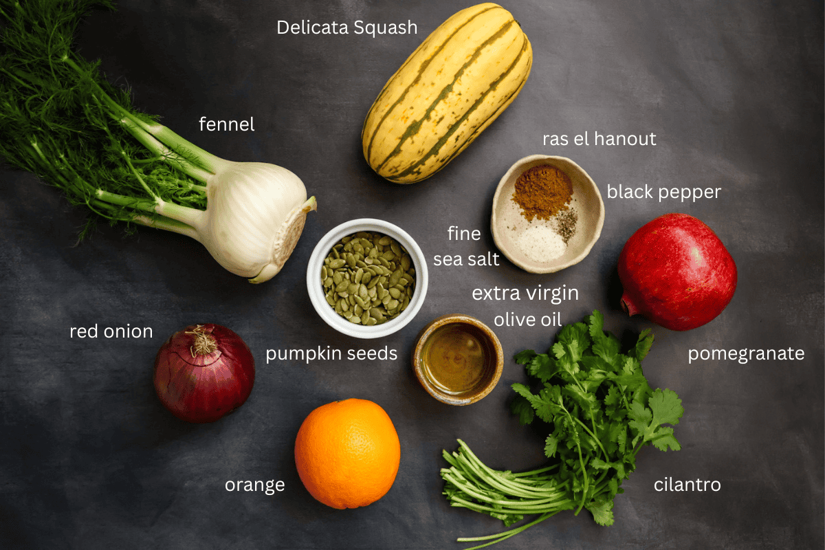 All the ingredients for roasted delicata squash and fennel salad with pomegranate seeds are arranged and labeled on a dark grey surface.