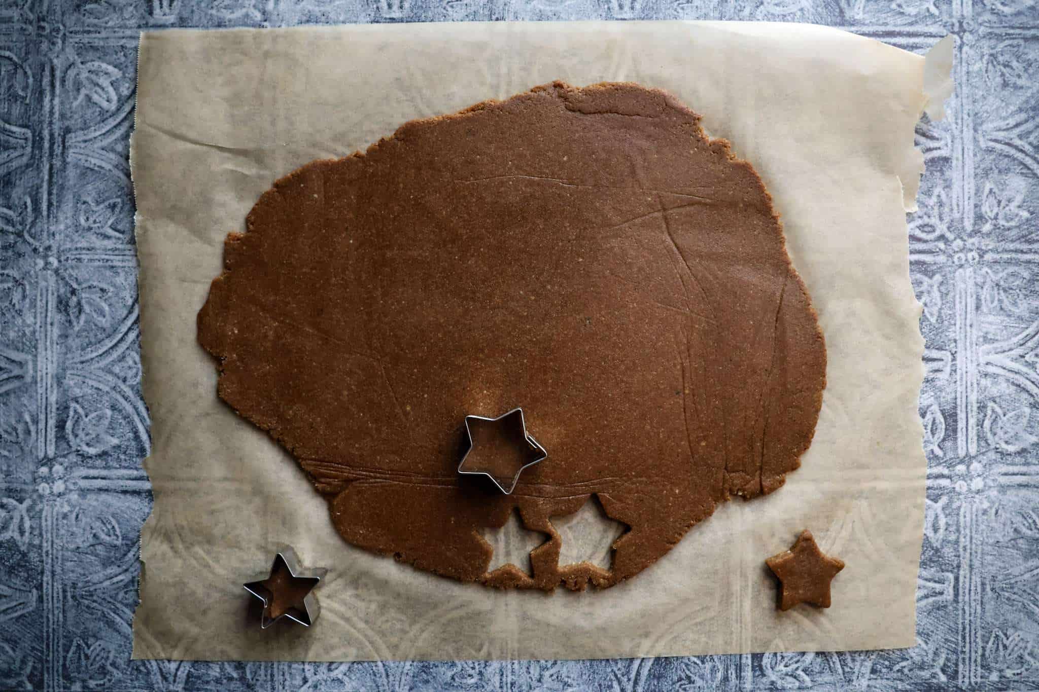 Rolled out dough for healthier zimtsterne with star cookie cutters - two cookies are already cut out and one is resting on the dough ready to be cut out