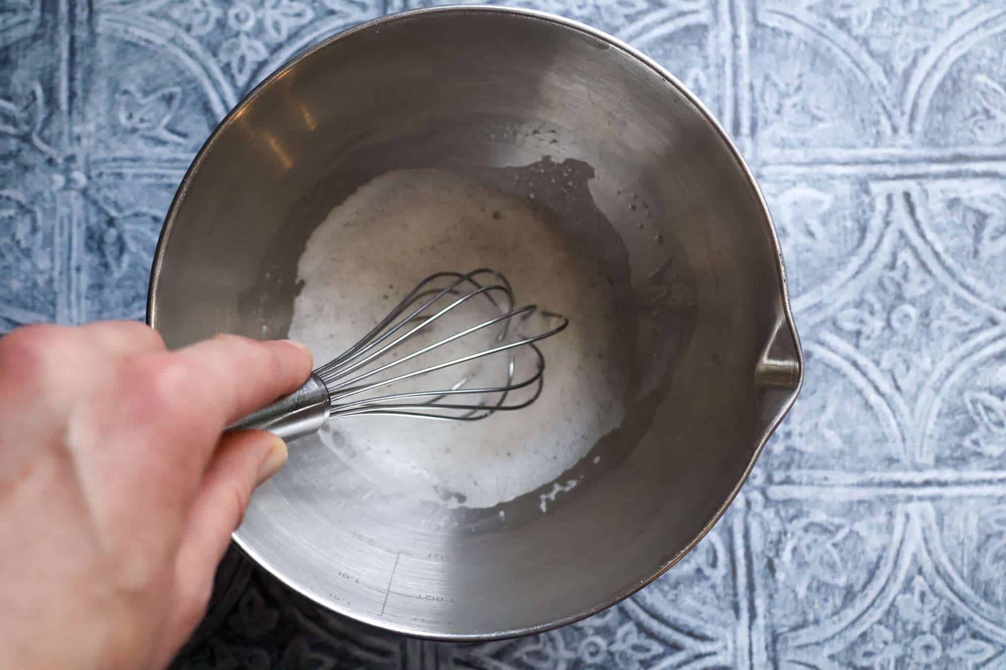 Am metal bowl with egg whites being whipped by hand with a whisk