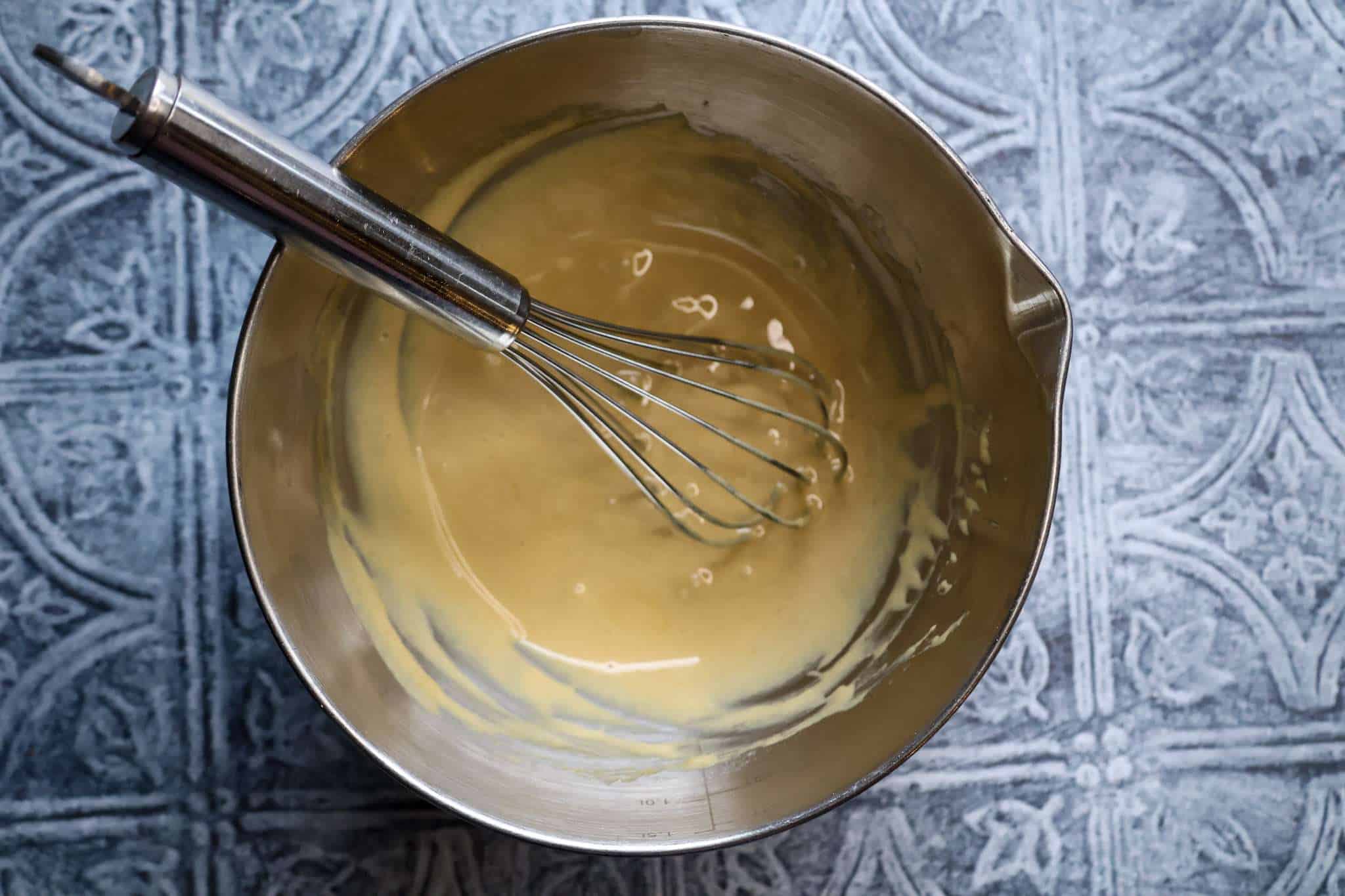 A meta bowl showing the glaze for healthier zimtsterne cookies with a whisk resting in the bowl