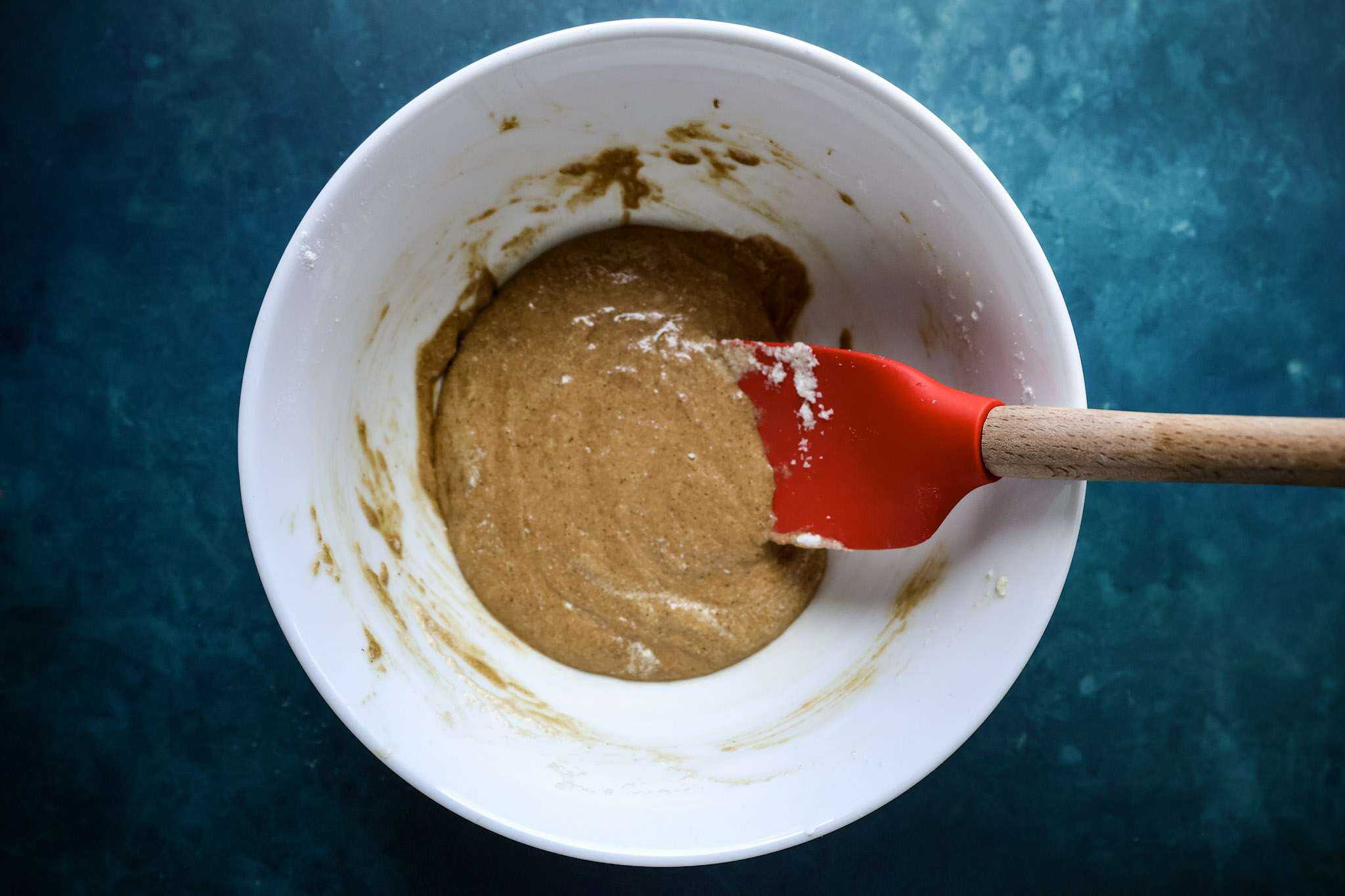 a while bowl with a red spatula resting inside and the batter for the cranberry tiramisu pie sponge with a little bit of egg white added into it