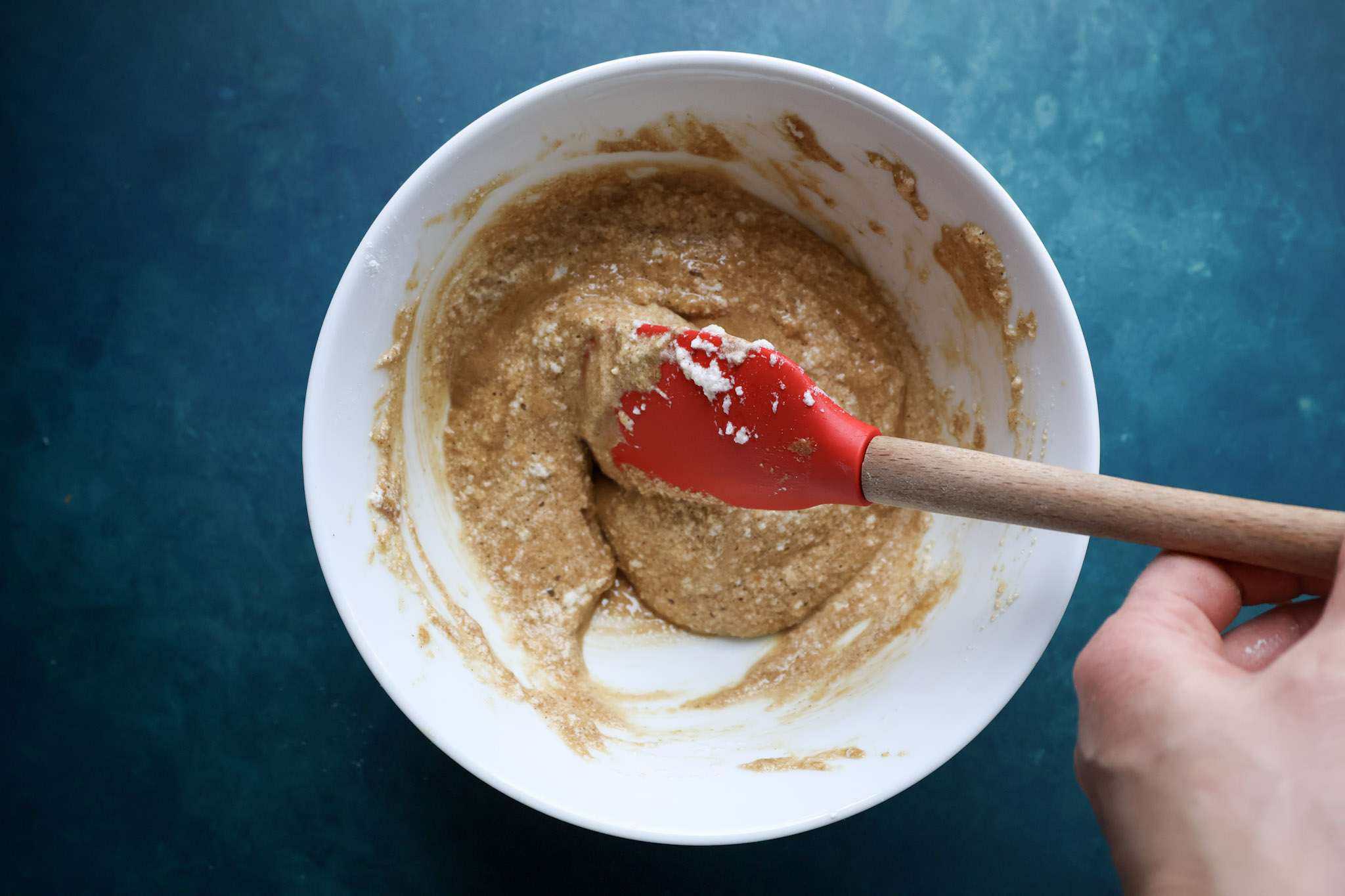 A whit bowl with the batter for the sponge for cranberry orange tiramisu pie with all the egg whites folded in and a red spatula can be seen used to fold in the egg whites