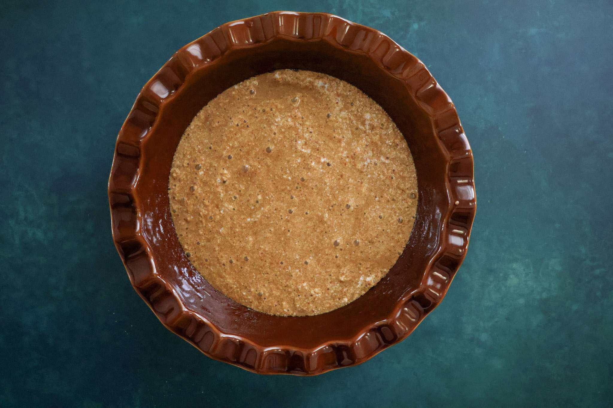 a brown pie dish with batter for the sponge for gluten-free cranberry orange tiramisu pie