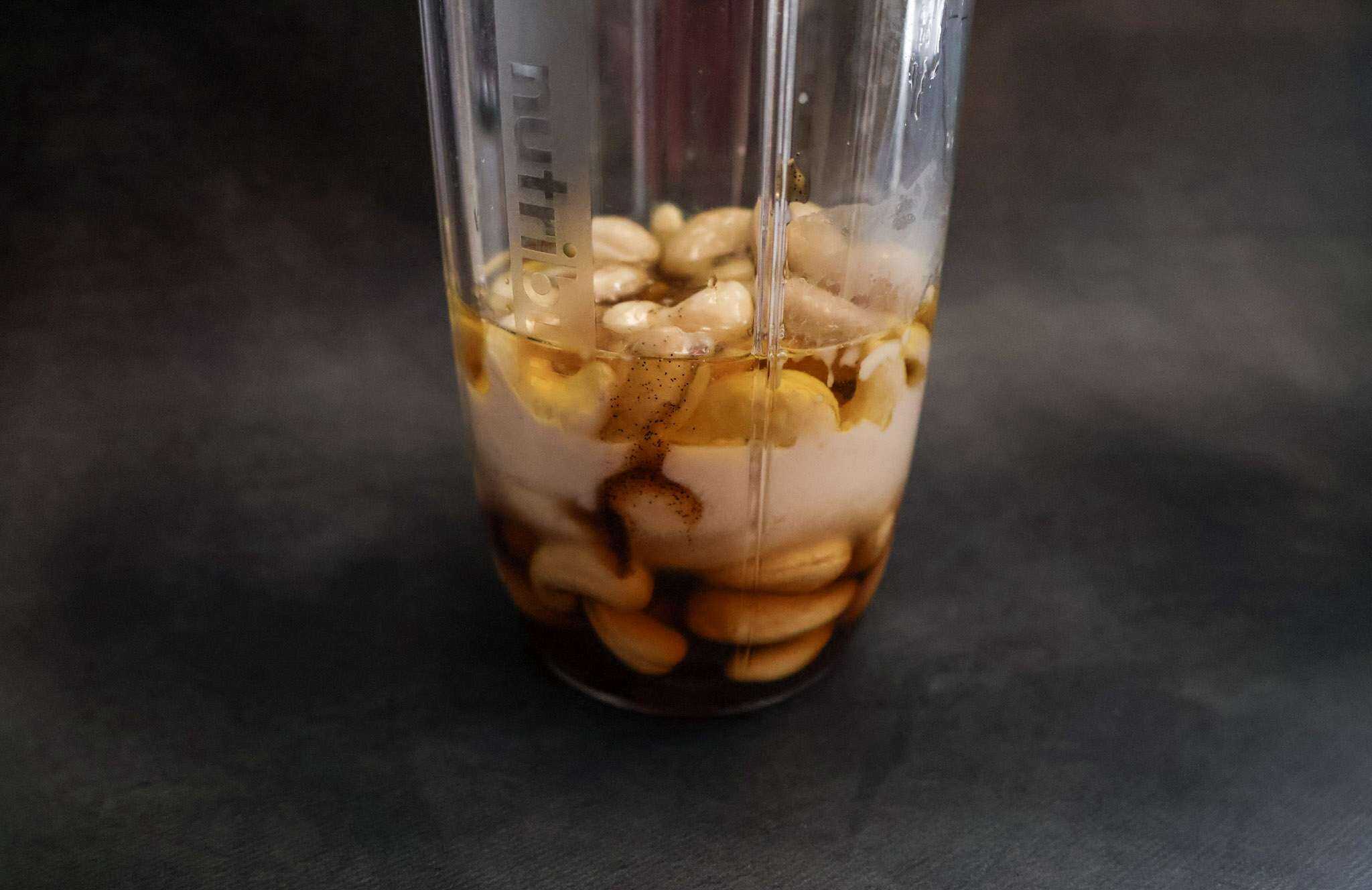 A blender jar with cashews, vanilla pasta, maple syrup, cacao butter, lemon juice, apple cider vinegar, salt and nut milk for dairy-free mascarpone-style frosting