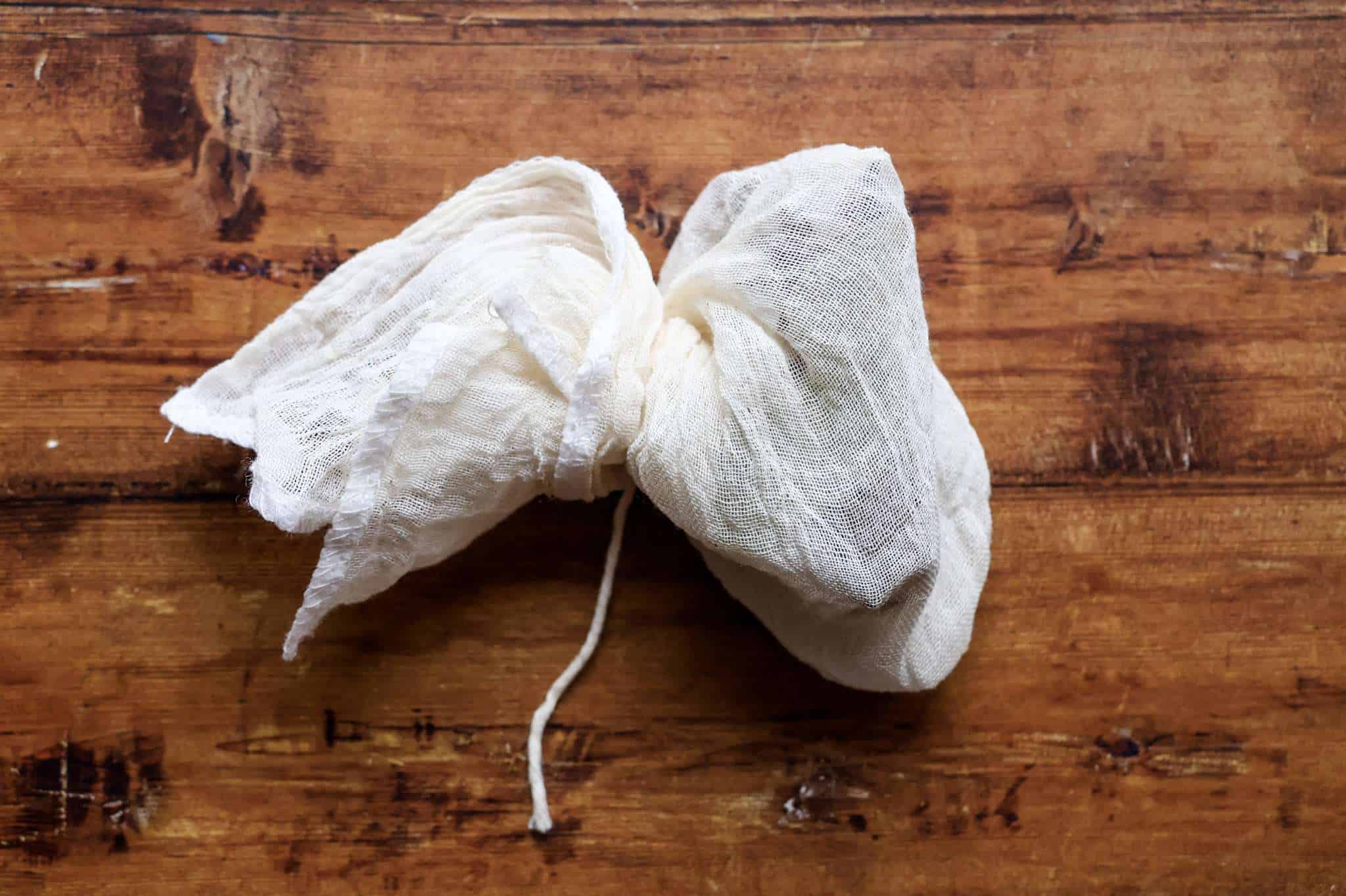 a little bag of cheese cloth tied with kitchen twin on a wooden surface
