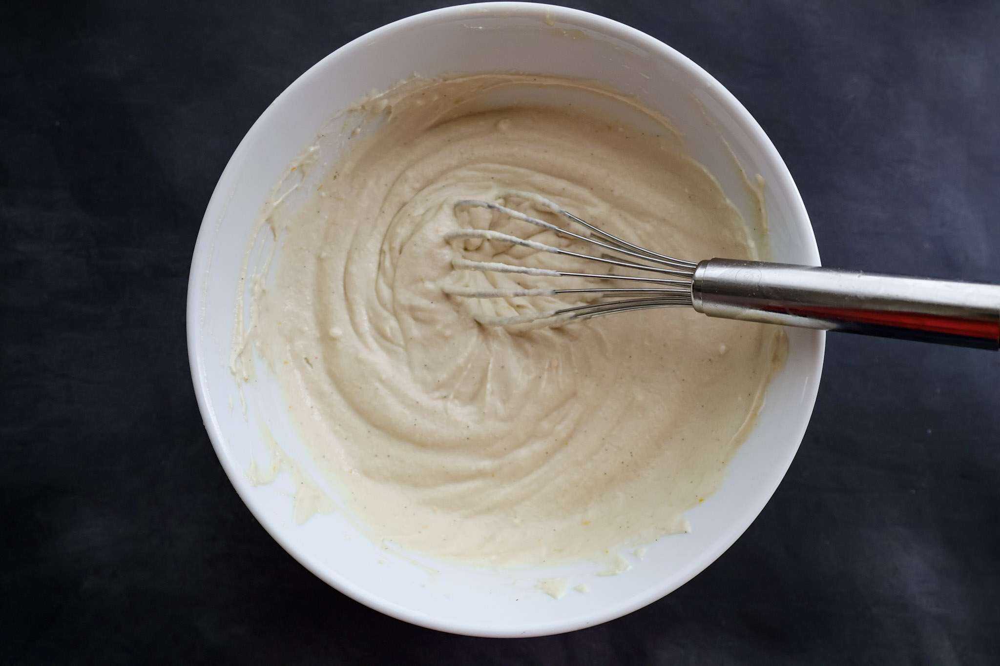 whisked dairy free mascarpone-style frosting in a white bowl with awhisk
