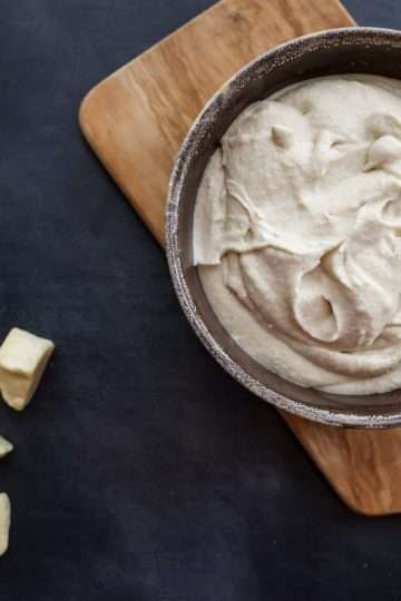 a bowl of dairy-free mascarpone-style frosting on a small wooden board and a few cacao butter chunks scattered in the forefront