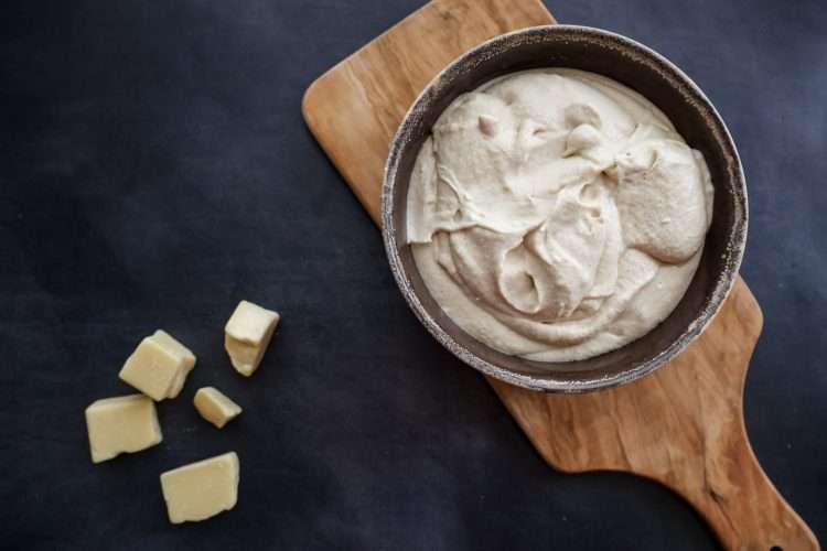 a bowl of dairy-free mascarpone-style frosting on a small wooden board and a few cacao butter chunks scattered in the forefront
