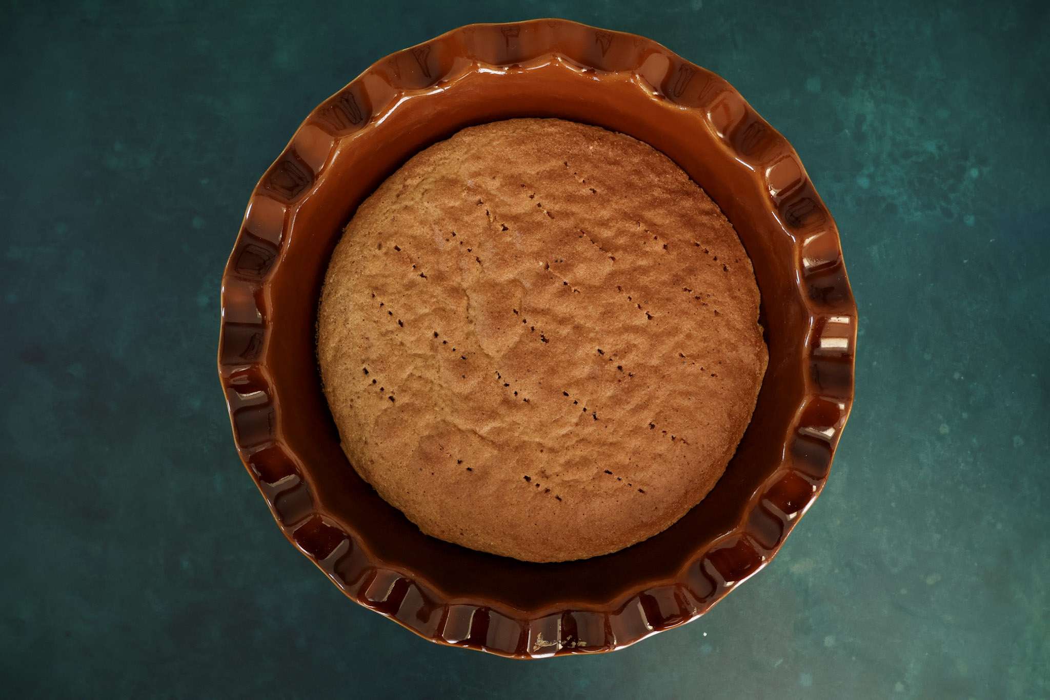 The baked sponge for cranberry tiramisu pie in a brown pie dish - the sponge was pierced all over with a fork