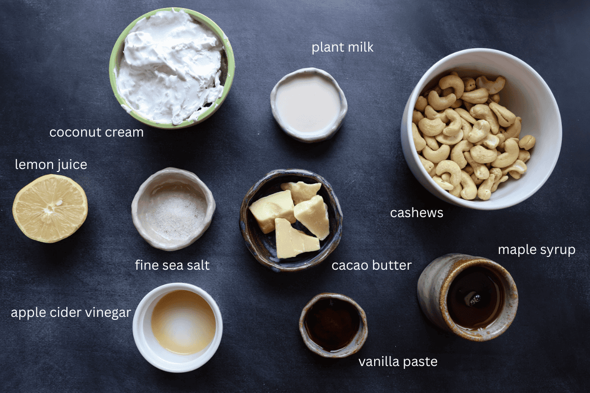 all ingredients for dairy-free mascarpone-style frosting are displayed in small bowls on a dark charcoal surface and labeled