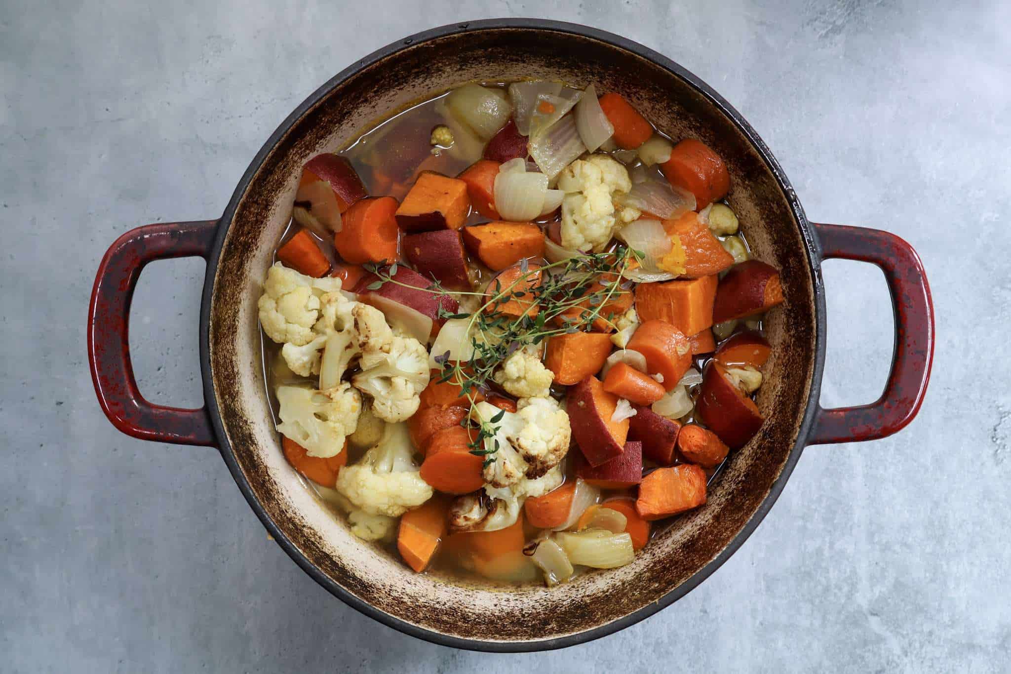A pot with roasted vegetables, broth and thyme for creamy winter vegetable soup prior to pureeing
