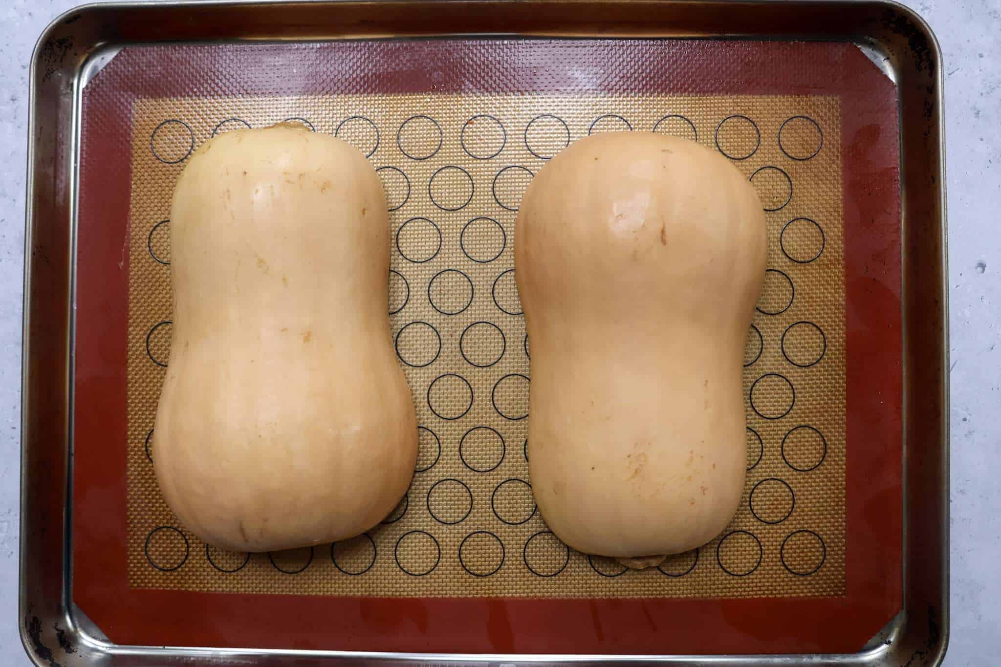 Two butternut squash halves, cut side down, on a baking sheet