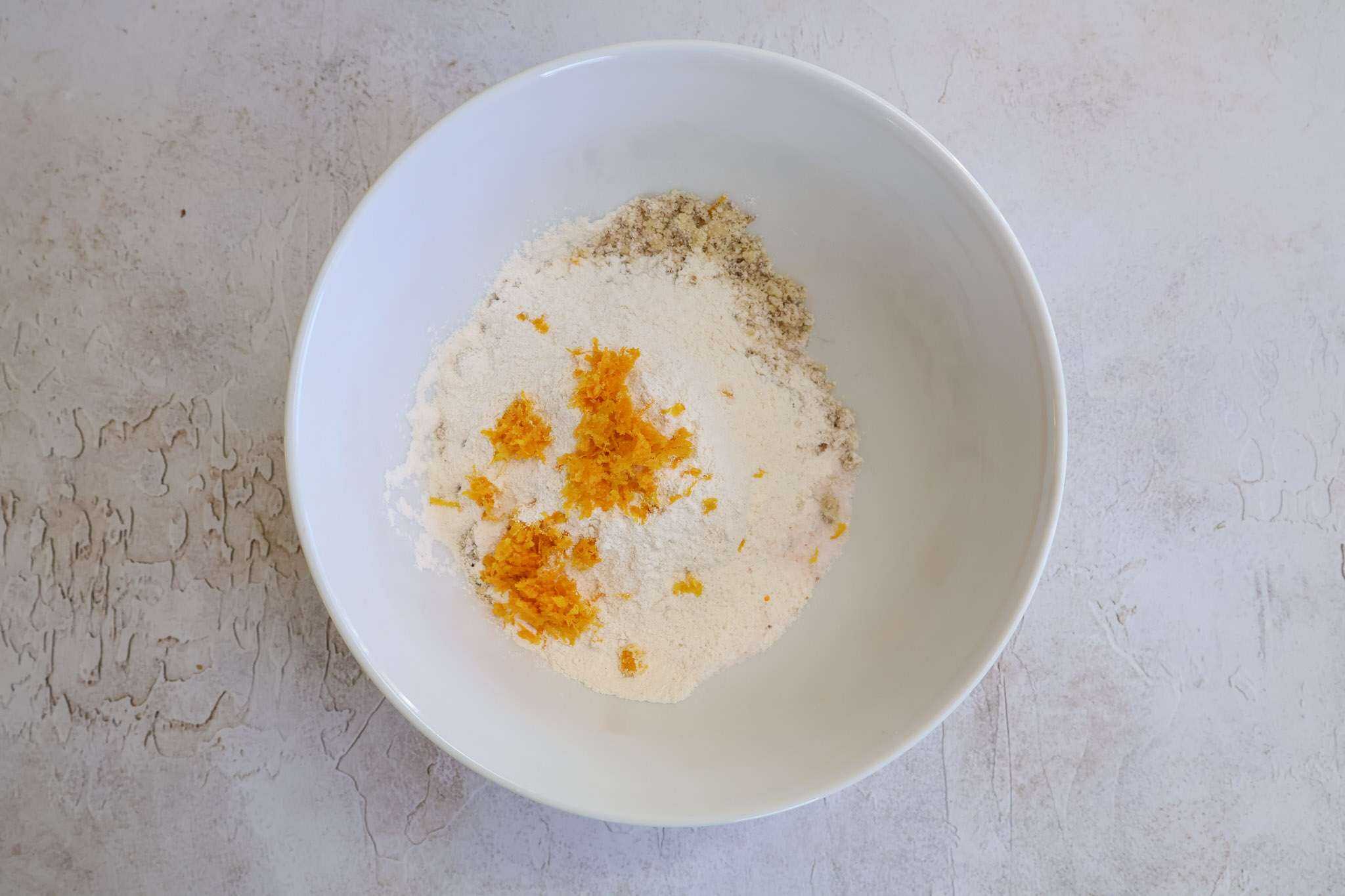Dry ingredients and orange zest for orange walnut frangipane style cakes in a white bowl