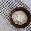 A brown bowl with easy coconut creme fraiche on a white and black striped kitchen towel