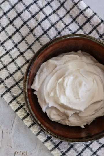 A brown bowl with easy coconut creme fraiche on a white and black striped kitchen towel