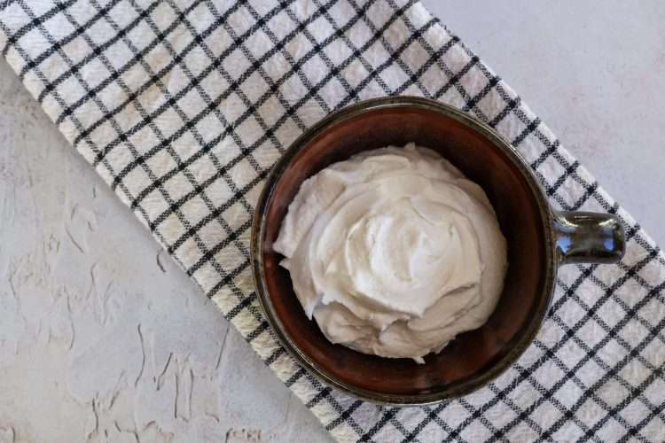 A brown bowl with easy coconut creme fraiche on a white and black striped kitchen towel