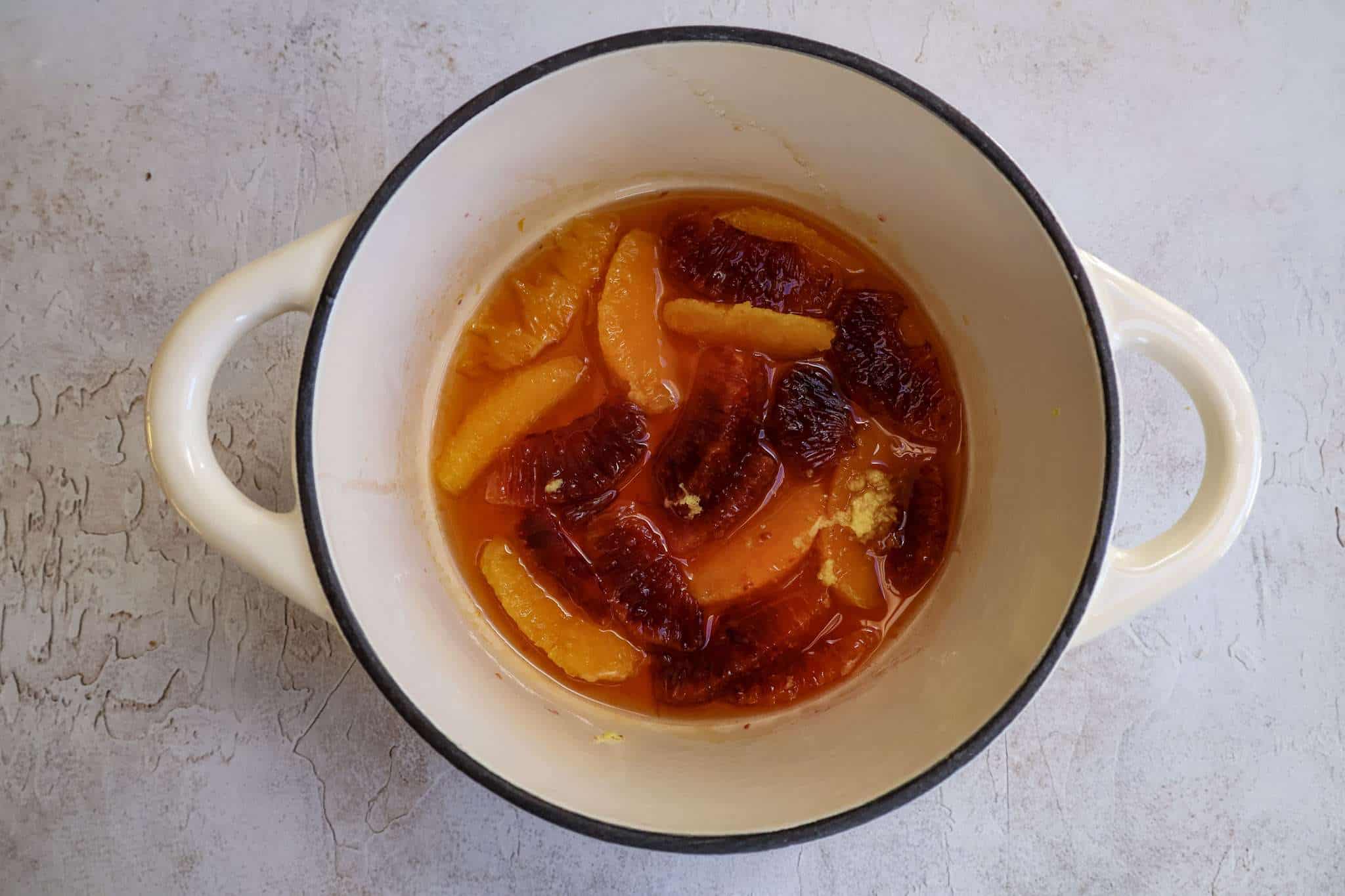 A small white Dutch oven pot with quick orange jam ready to cook