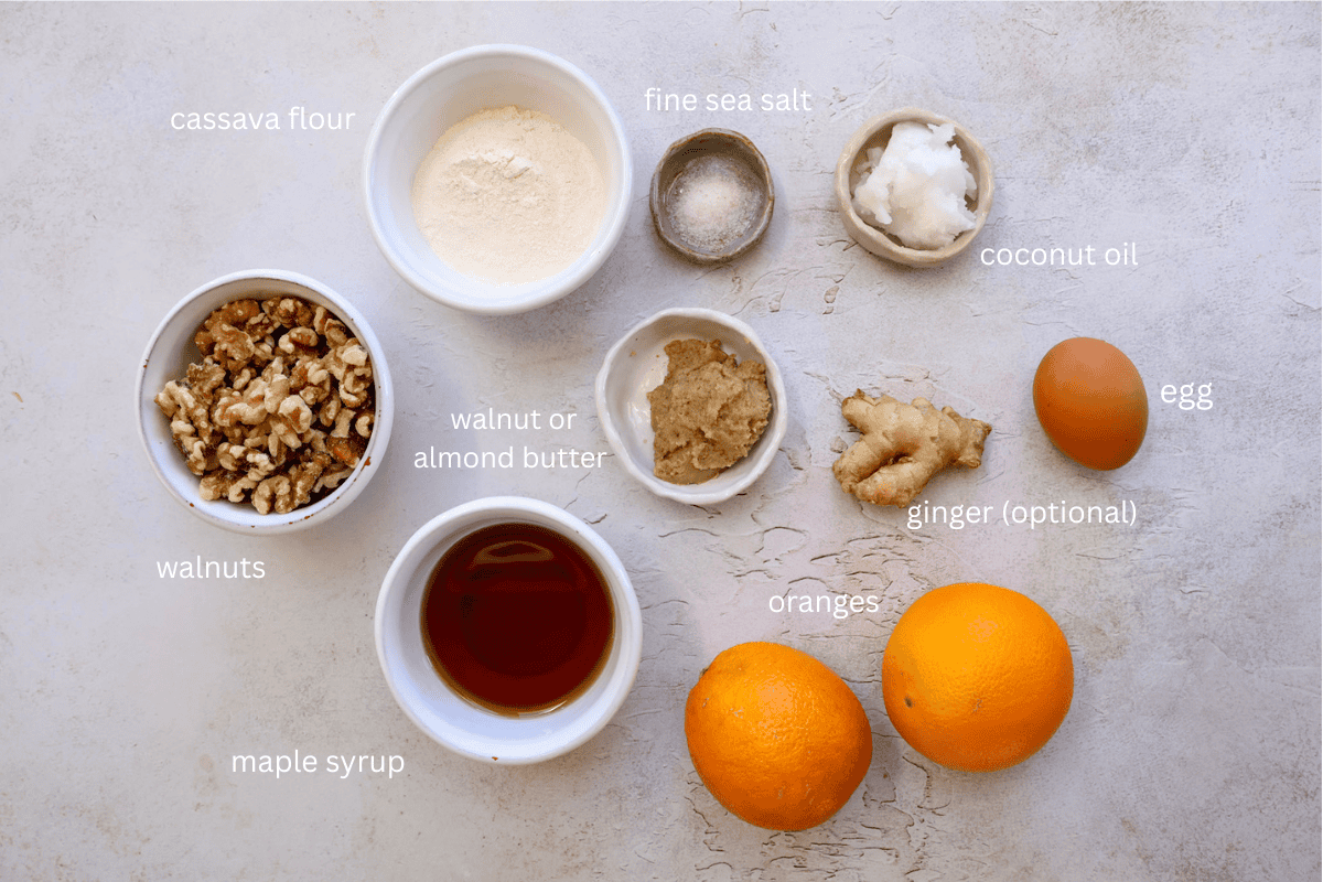 All ingredients for orange walnut frangipane style cakes are displayed on a concrete style surface and labeled