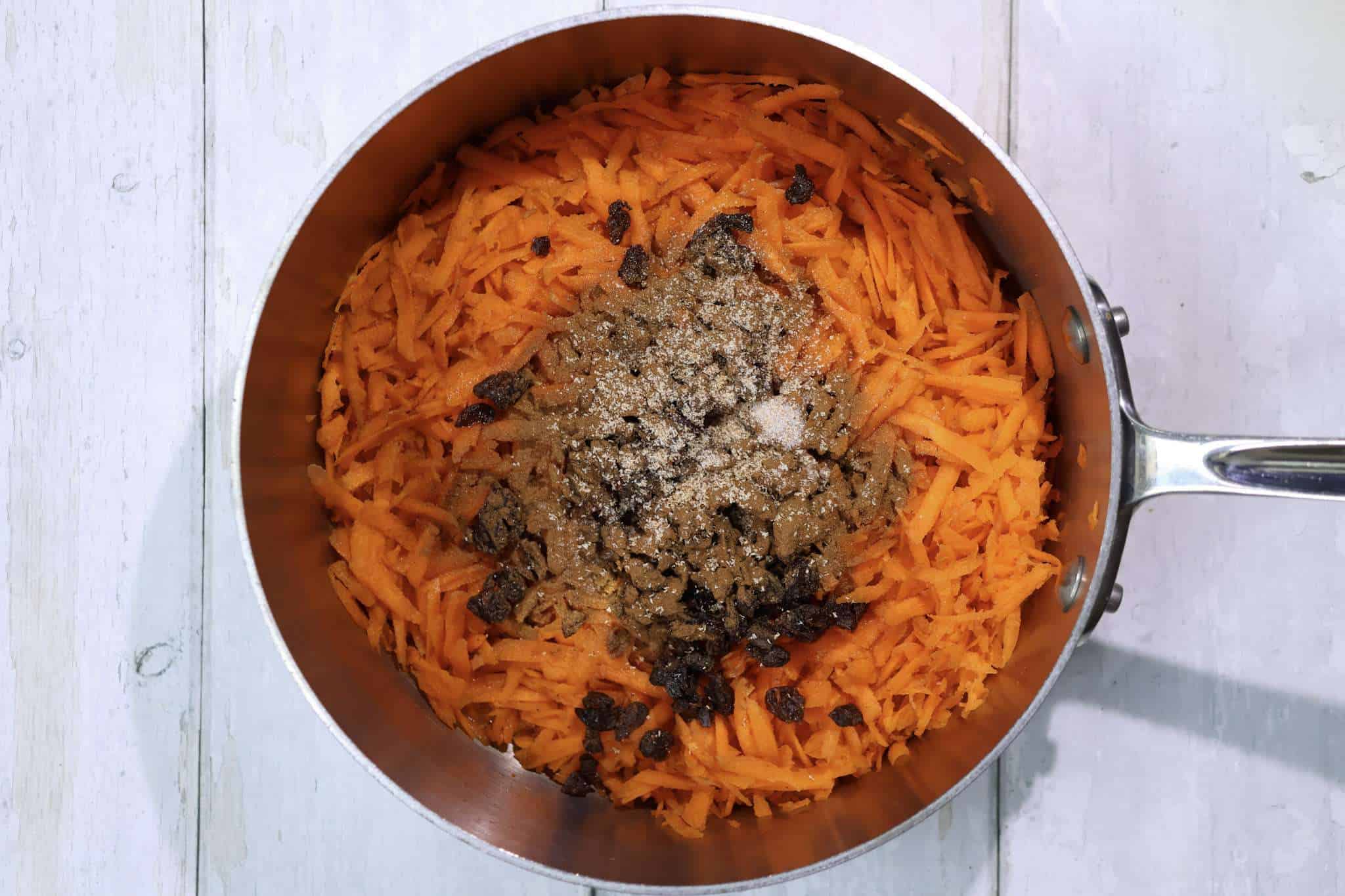 Grated carrots, maple syrup, orange juice, raisins, cinnamon, nutmeg, and salt for carrot cake crepe filling in a pot