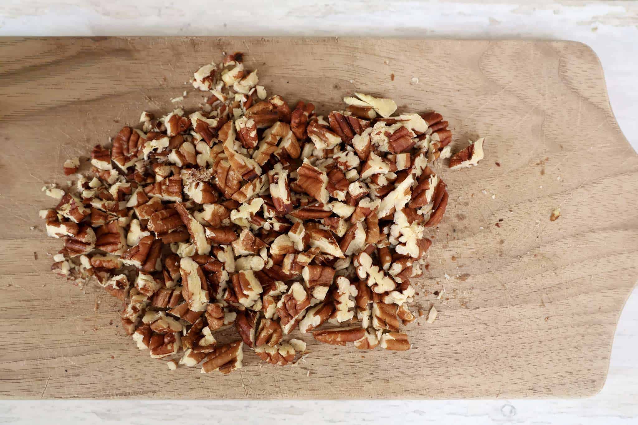 Chopped, toasted pecans on a wooden board