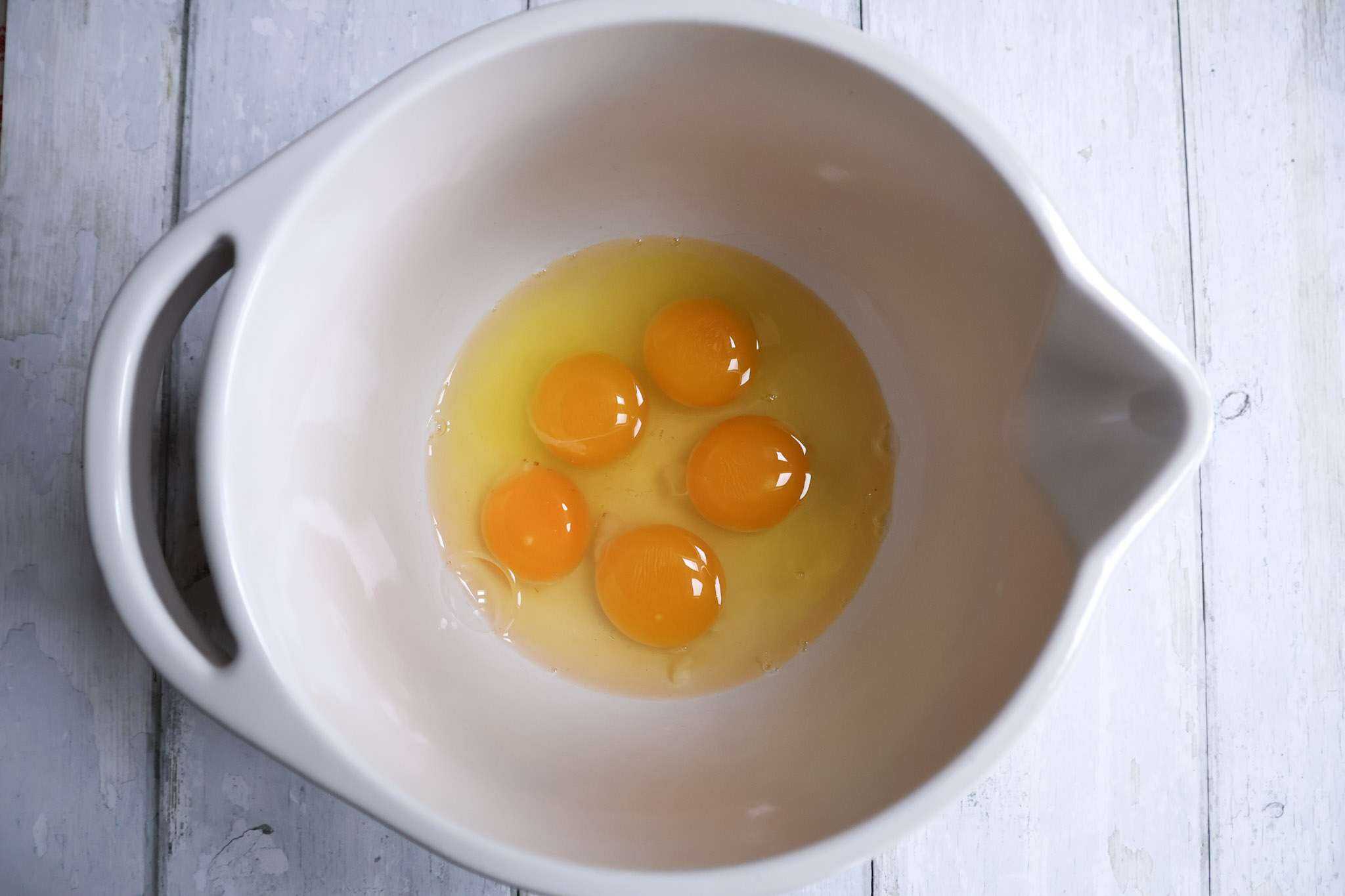 5 cracked eggs in a white bowl