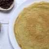 A white plate with crepes and small bowls of maple syrup and raisins are off to the left side