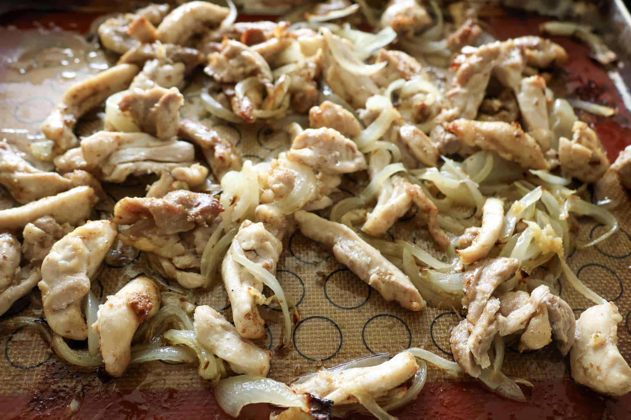 A sheet pan with roasted and thinly sliced onions and chicken thighs