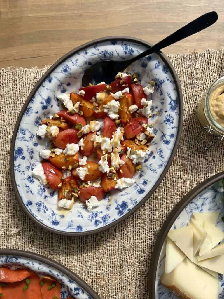 A white and blue platter with grilled apricots, crumbled goat cheese, chopped pistachios and honey