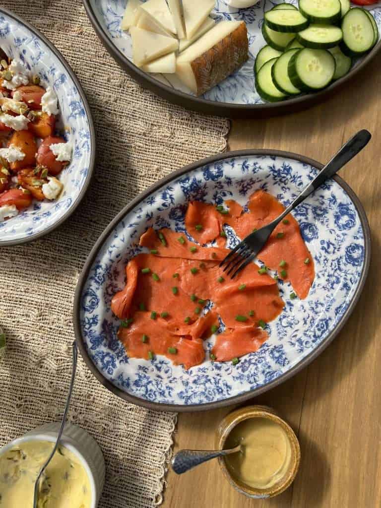 A blue and white platter with smoked salmon and chopped chives and a vegetable platter and grilled apricots in the background