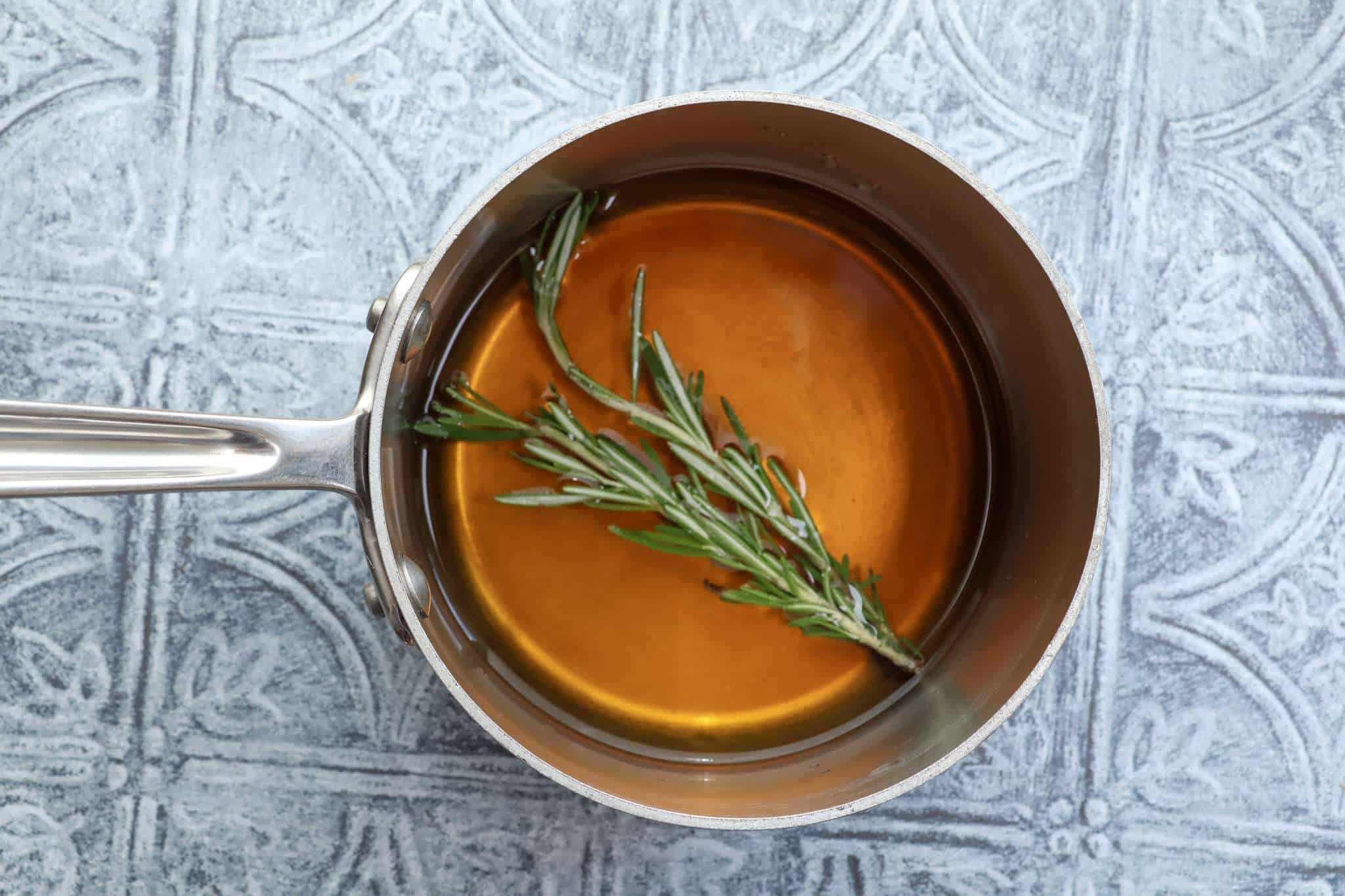 A stainless steel pot with a water and maple syrup mixture and two rosemary sprigs
