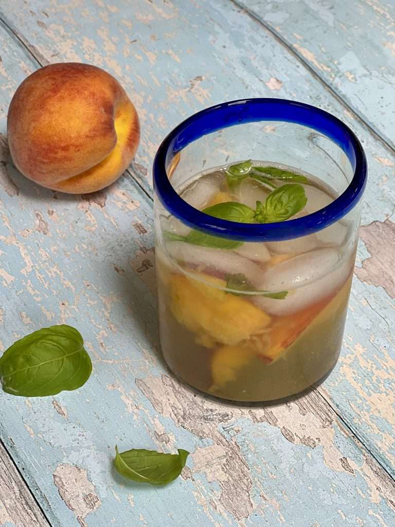 peach basil refresher in glass with blue rim, a peach and a basil leaf in the background