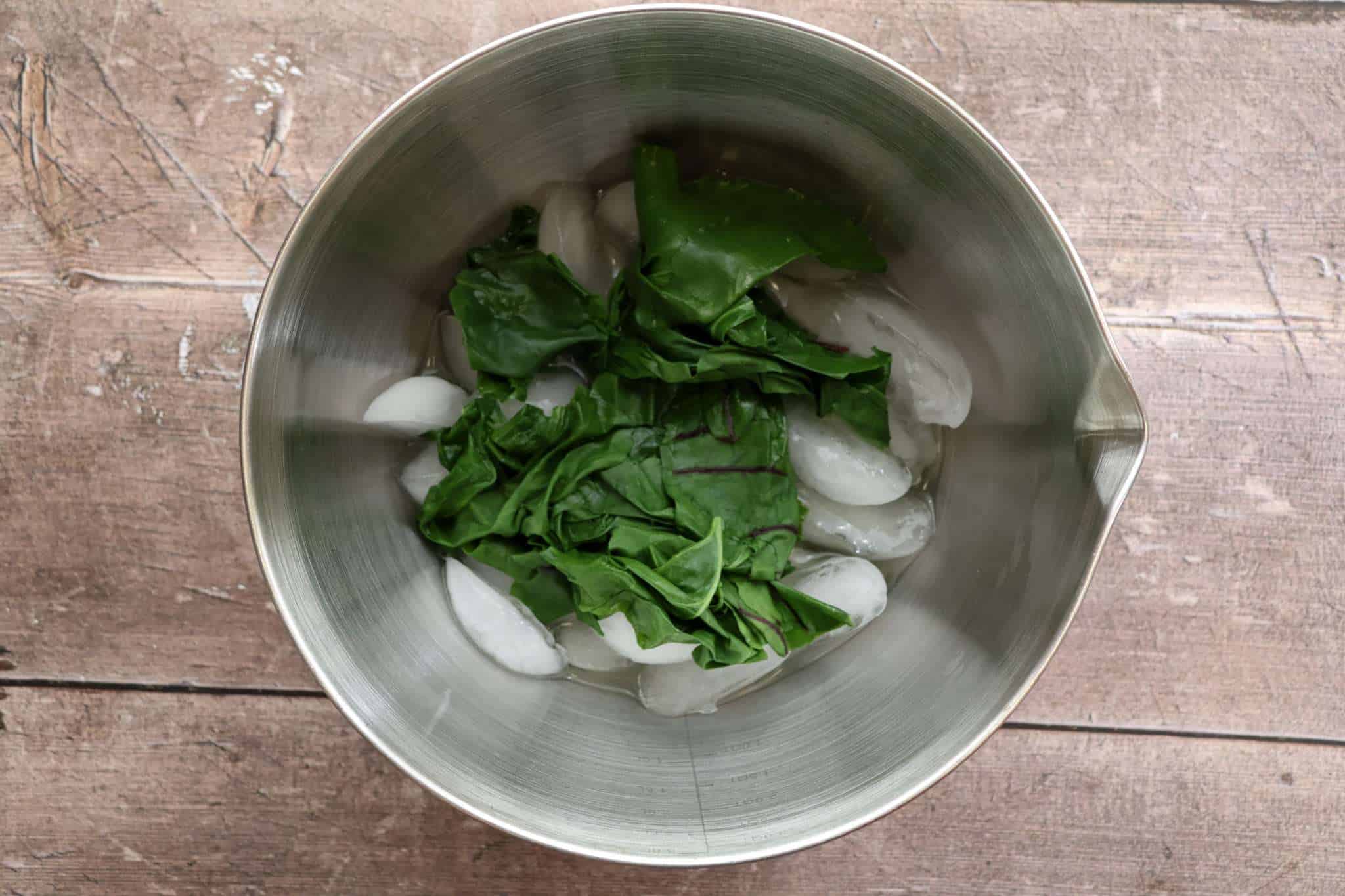 A metal mixing bowl with blanched beet greens in an ice bath