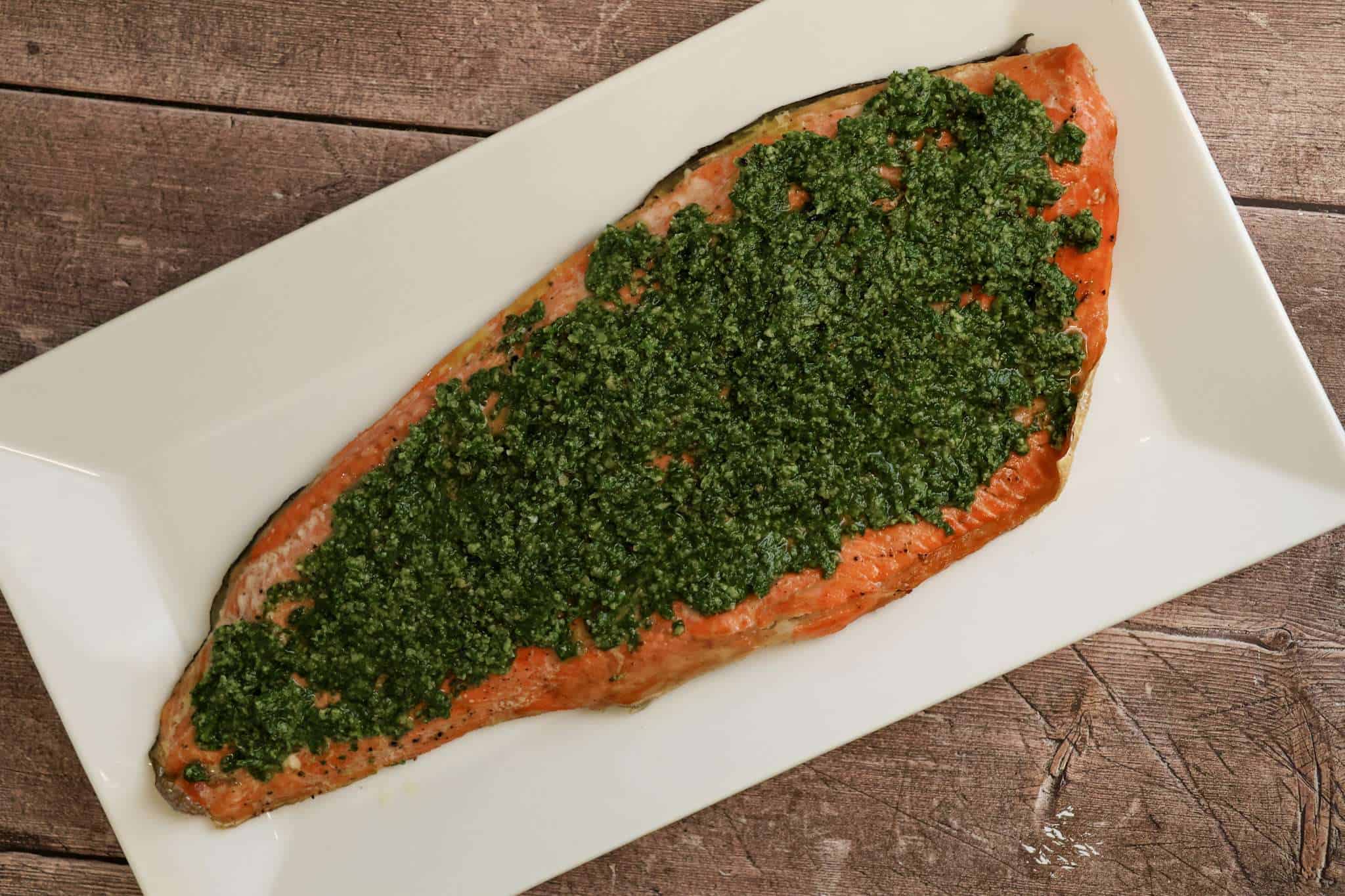 A salmon fillet topped with beet green gremolata on a rectangular white serving board