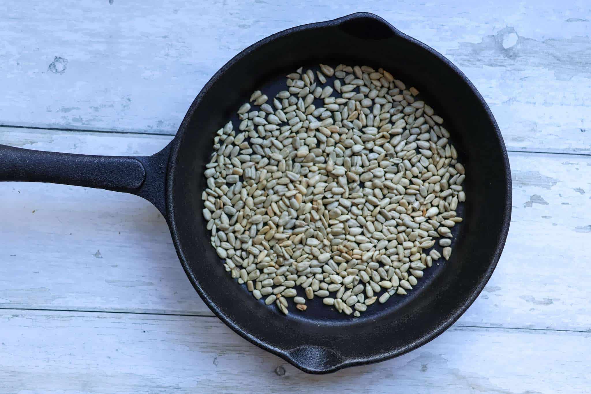 A cast iron pan with sunflower seeds toasting in it