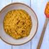A pottery bowl filled with carrot garlic scape pesto and a spatula resting next to it