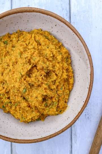 A pottery bowl filled with carrot garlic scape pesto and a spatula resting next to it
