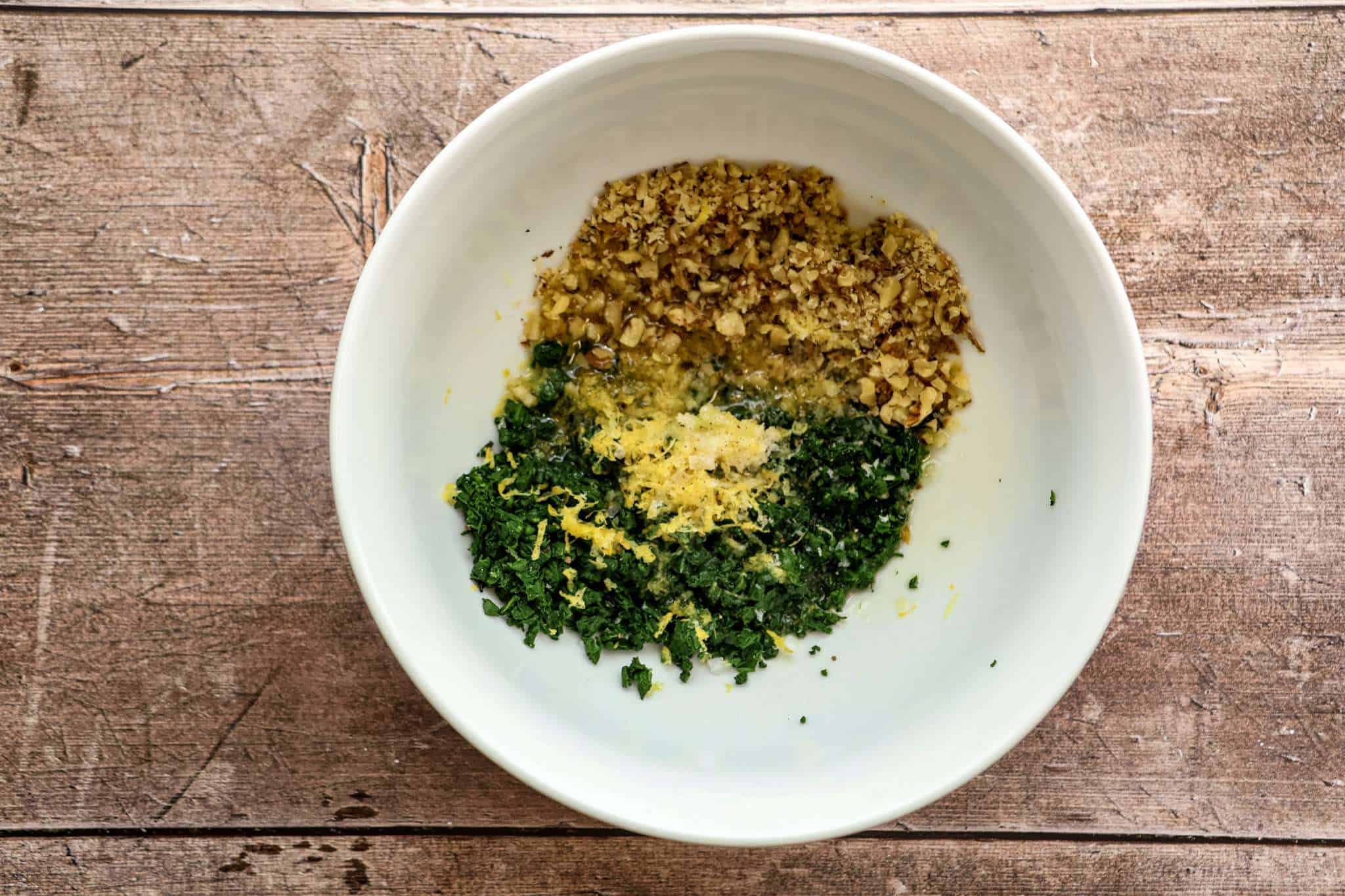 All ingredients for beet green gremolata in a white bowl on a wooden surface