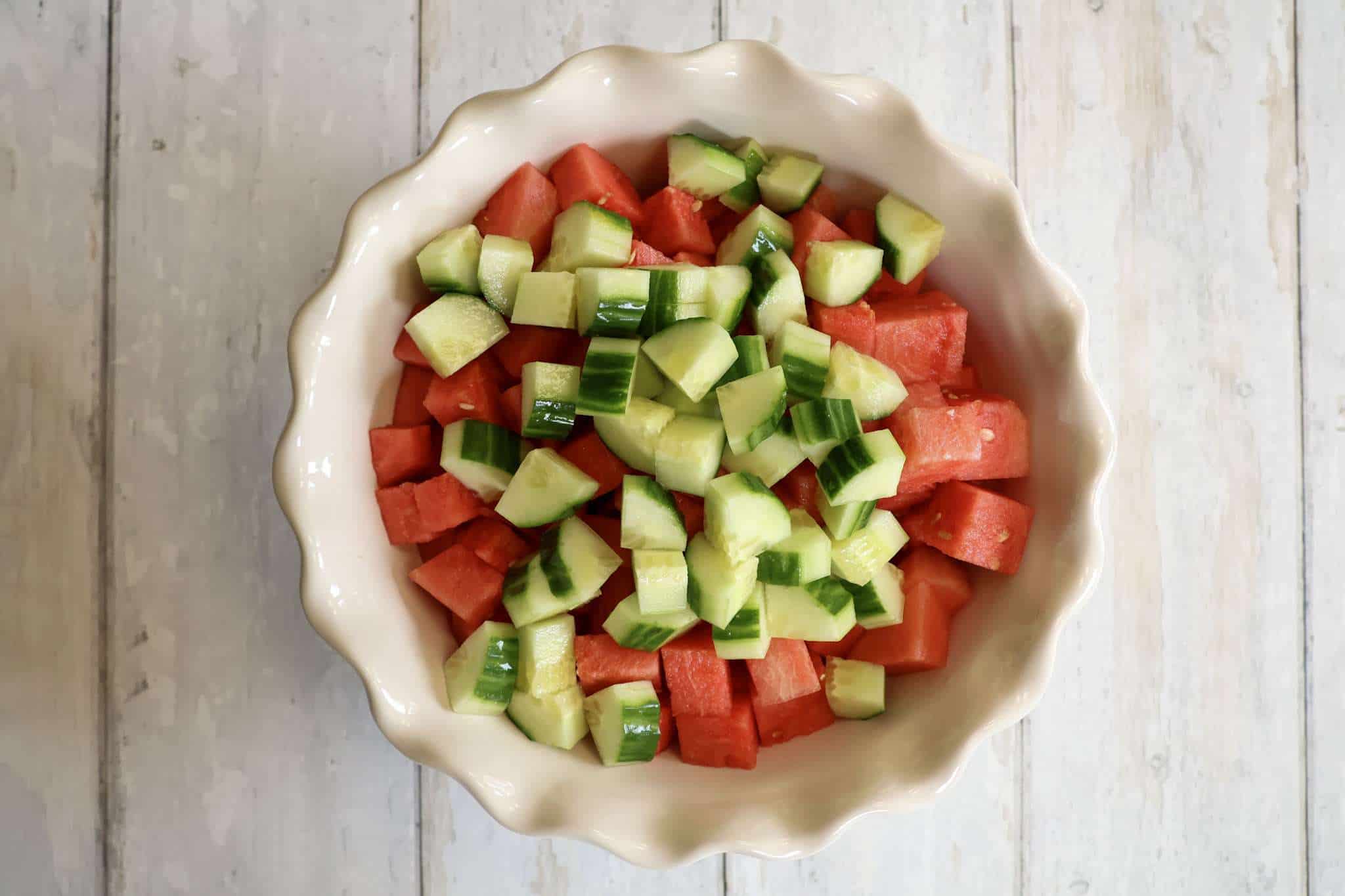 A white bowl filled with cubed watermelon and cucumber