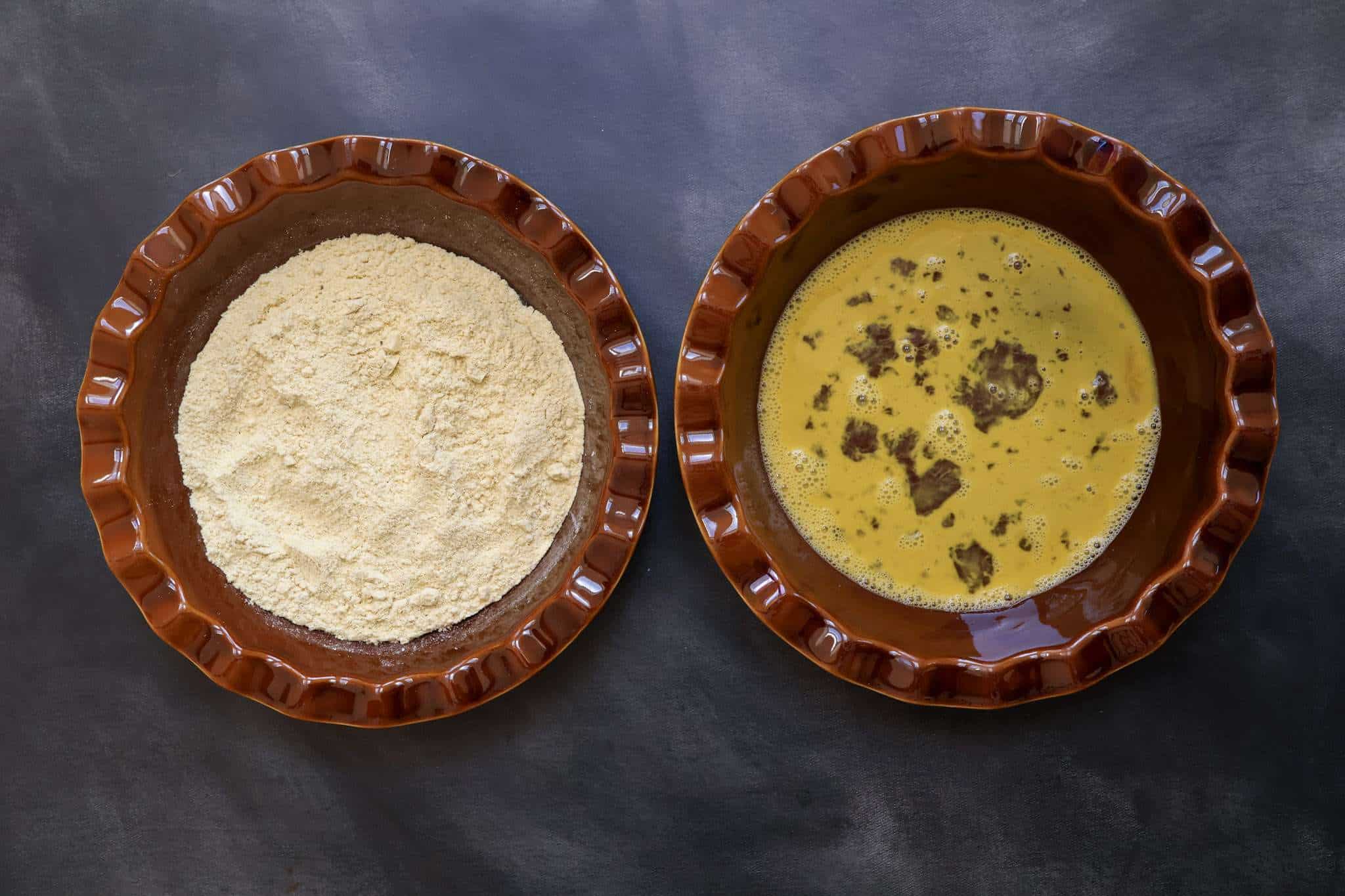two brown pie dishes - one holding an egg wash and the other a mixture of corn flour and ground sunflower seeds for breading a schnitzel
