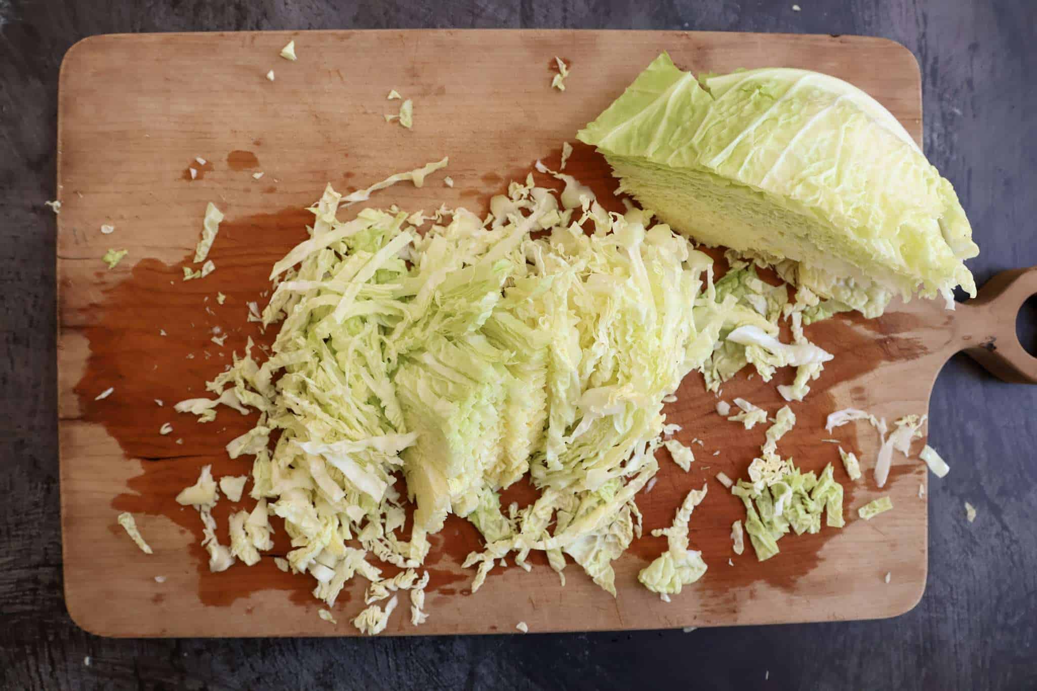 A savoy cabbage partially thinly sliced on a wooden board