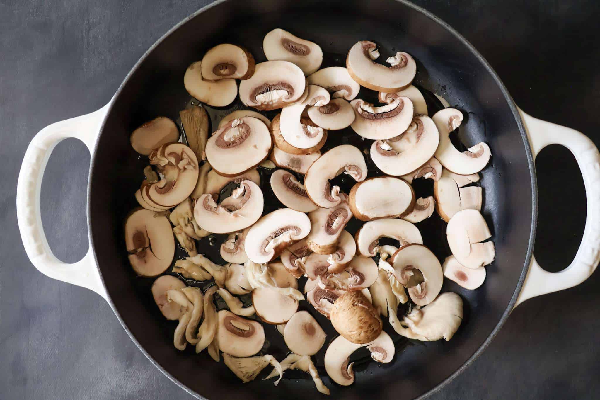 A white enameled cast iron pan with sliced button mushrooms