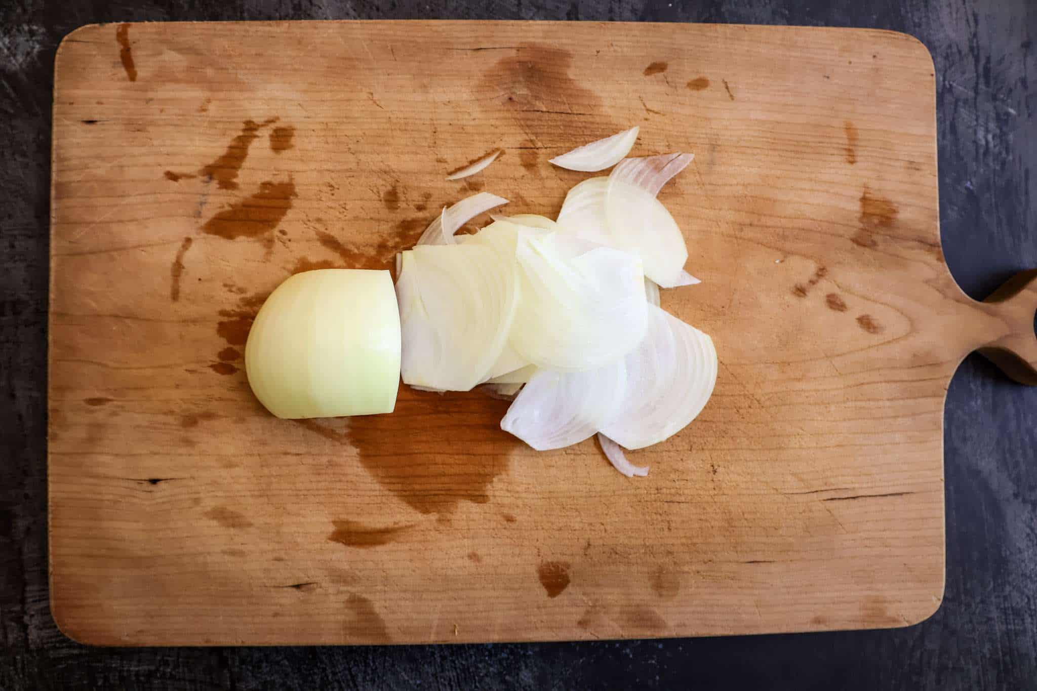 half a yellow onion is partially thinly sliced on a wooden board