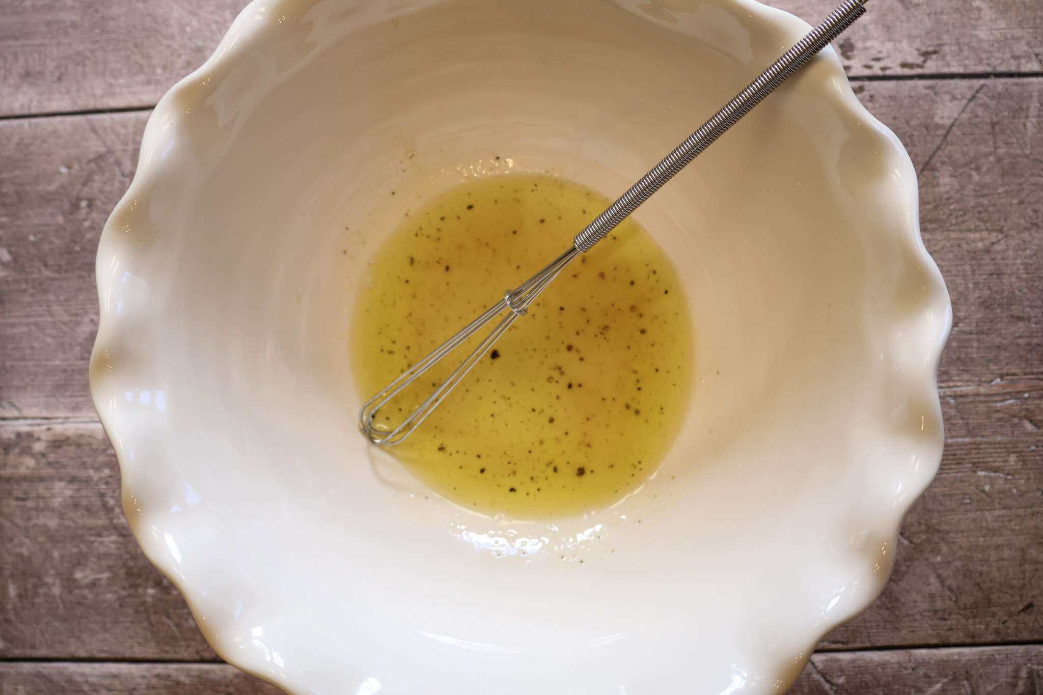 A white bowl with a light dressing and a small whisk resting in it