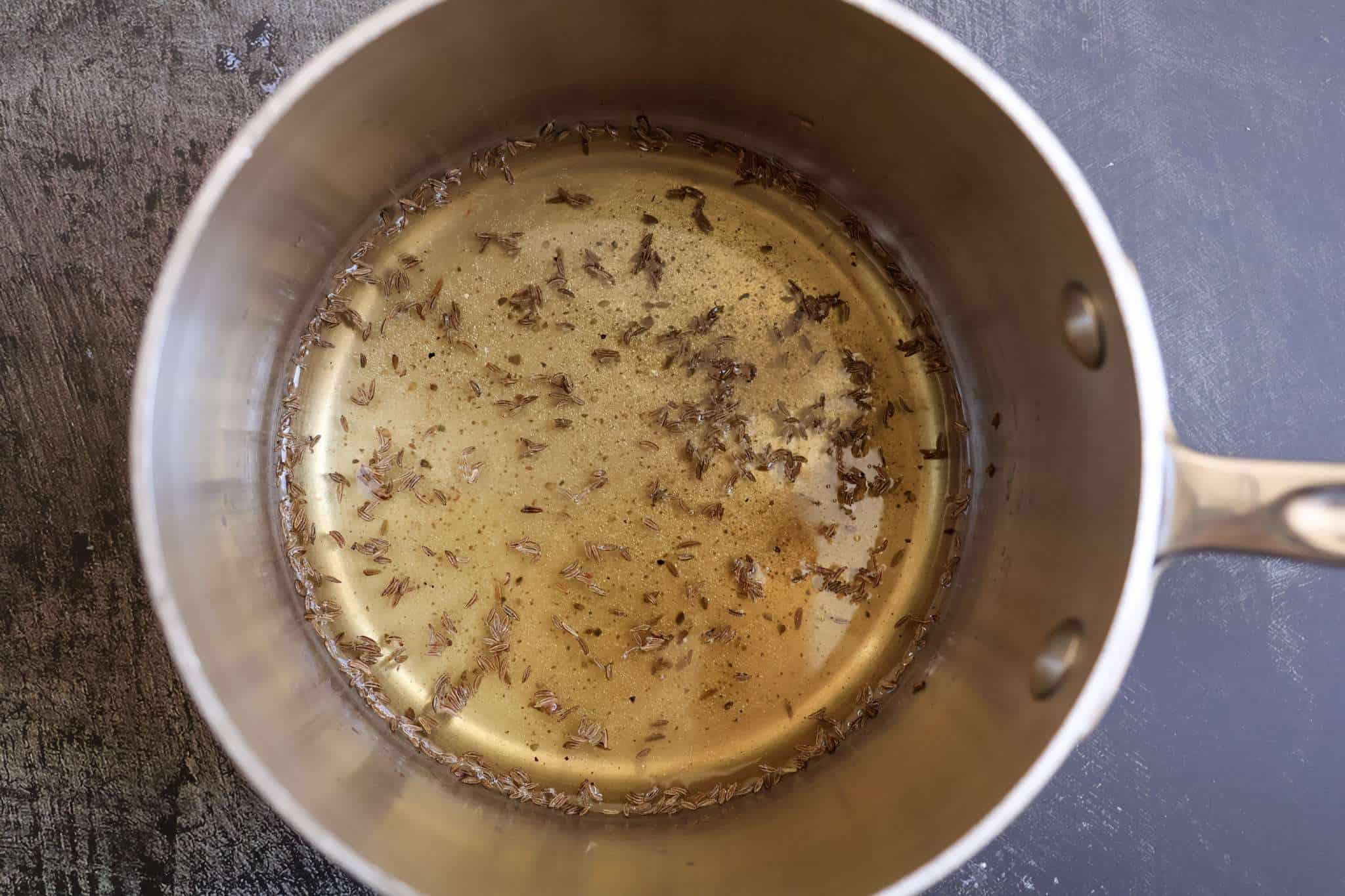 The warmed dressing for German krautsalat with caraway seeds in a small stainless steel pot