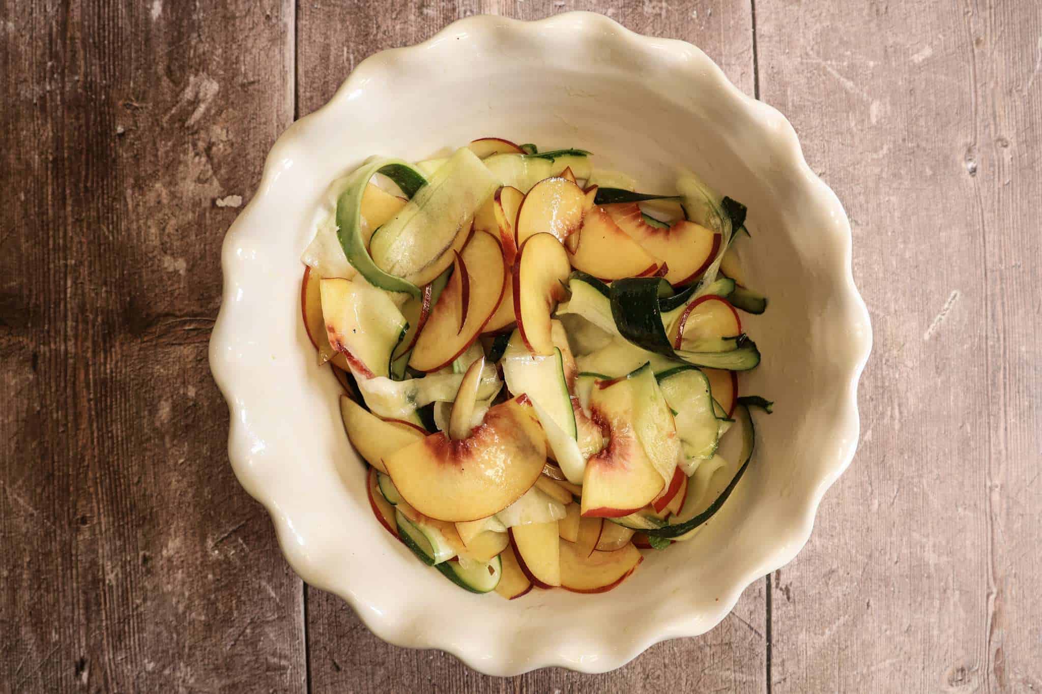 a white bowl with thinly sliced peaches and zucchini ribbons