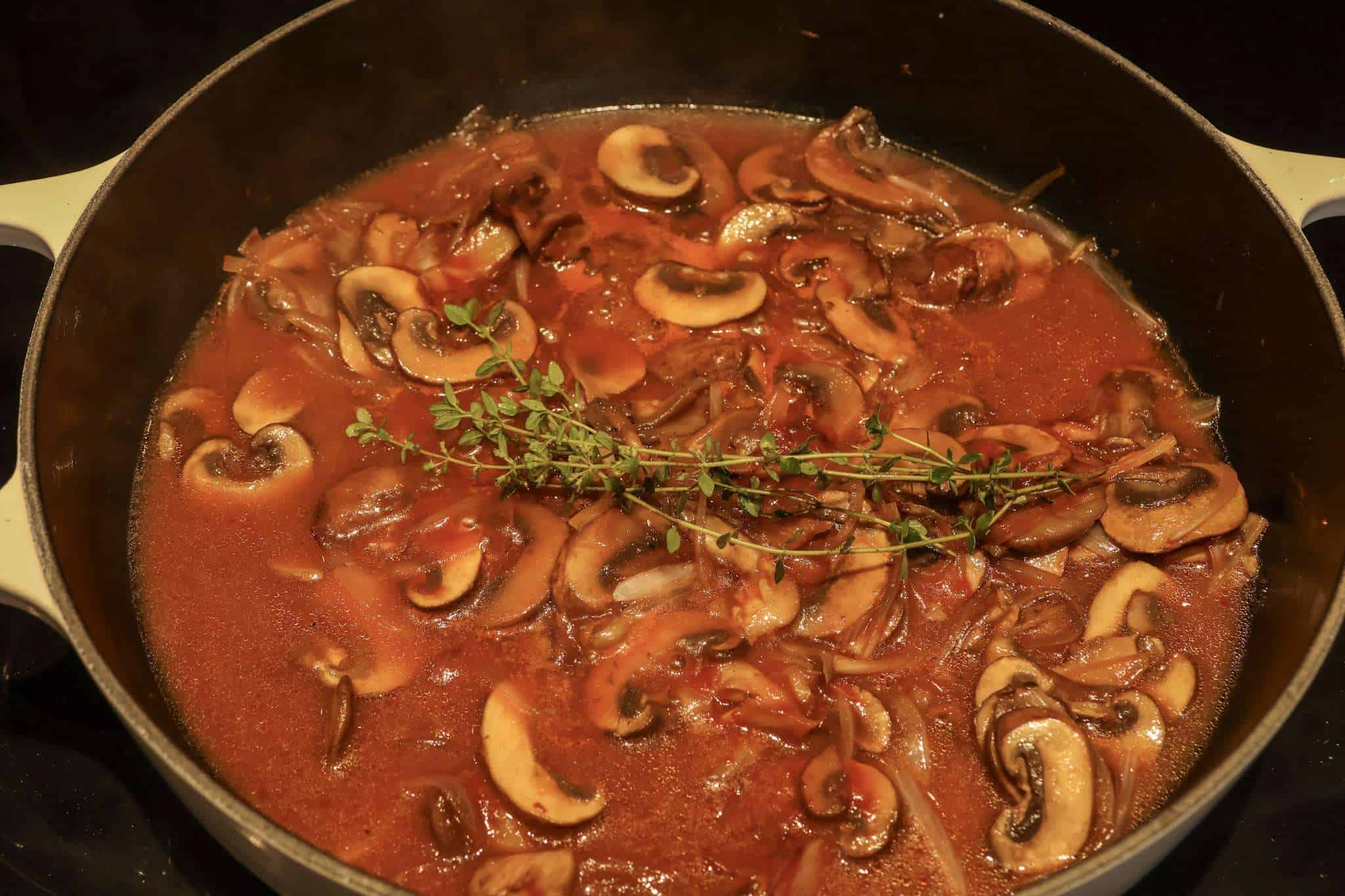 A white enameled cast iron pan with mushroom sauce for jaegerschnitzel cooking on a stove top