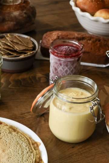 A variety of foods - sourdough bread, rolls, apple cake, granola, hummus, chia jam, crackers, pesto, crepes - displayed on a table
