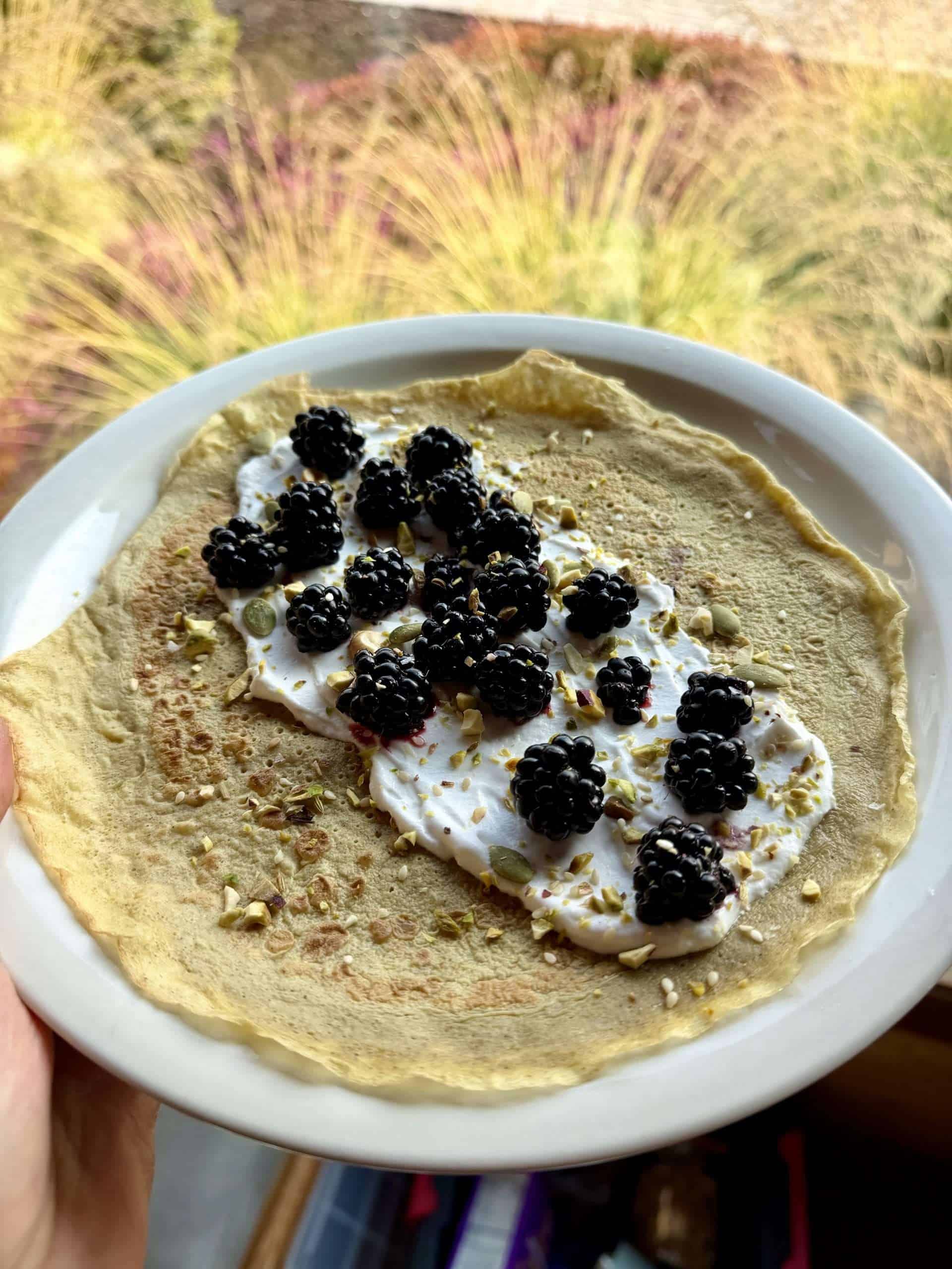 A crepe with yogurt, blackberries, and nuts and seeds on a white plate